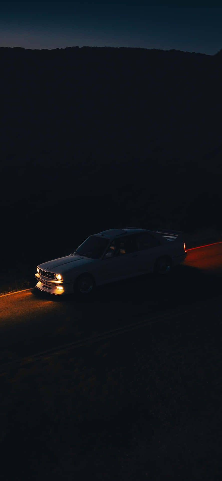  壁紙 — 一輛銀色汽車在夜間獨自行駛在一條黑暗蜿蜒的道路上，閃亮的車頭燈劃破陰影。