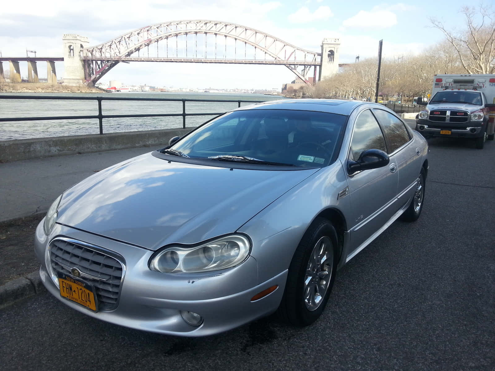 Chrysler Lhs 桌布 壁紙 — 一輛銀色克萊斯勒轎車停在海濱，身後有一座大型鋼拱橋橫跨河流。