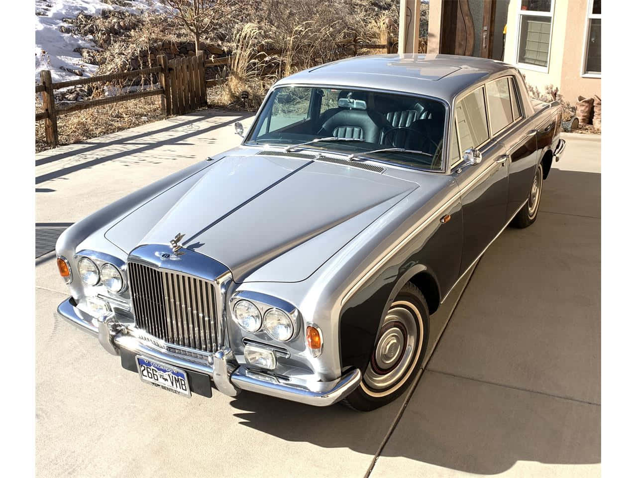 Bentley T1 桌布 壁紙 — 一輛閃亮的銀色經典賓利轎車停在混凝土車道上，背景是白雪覆蓋的山丘和乾草。