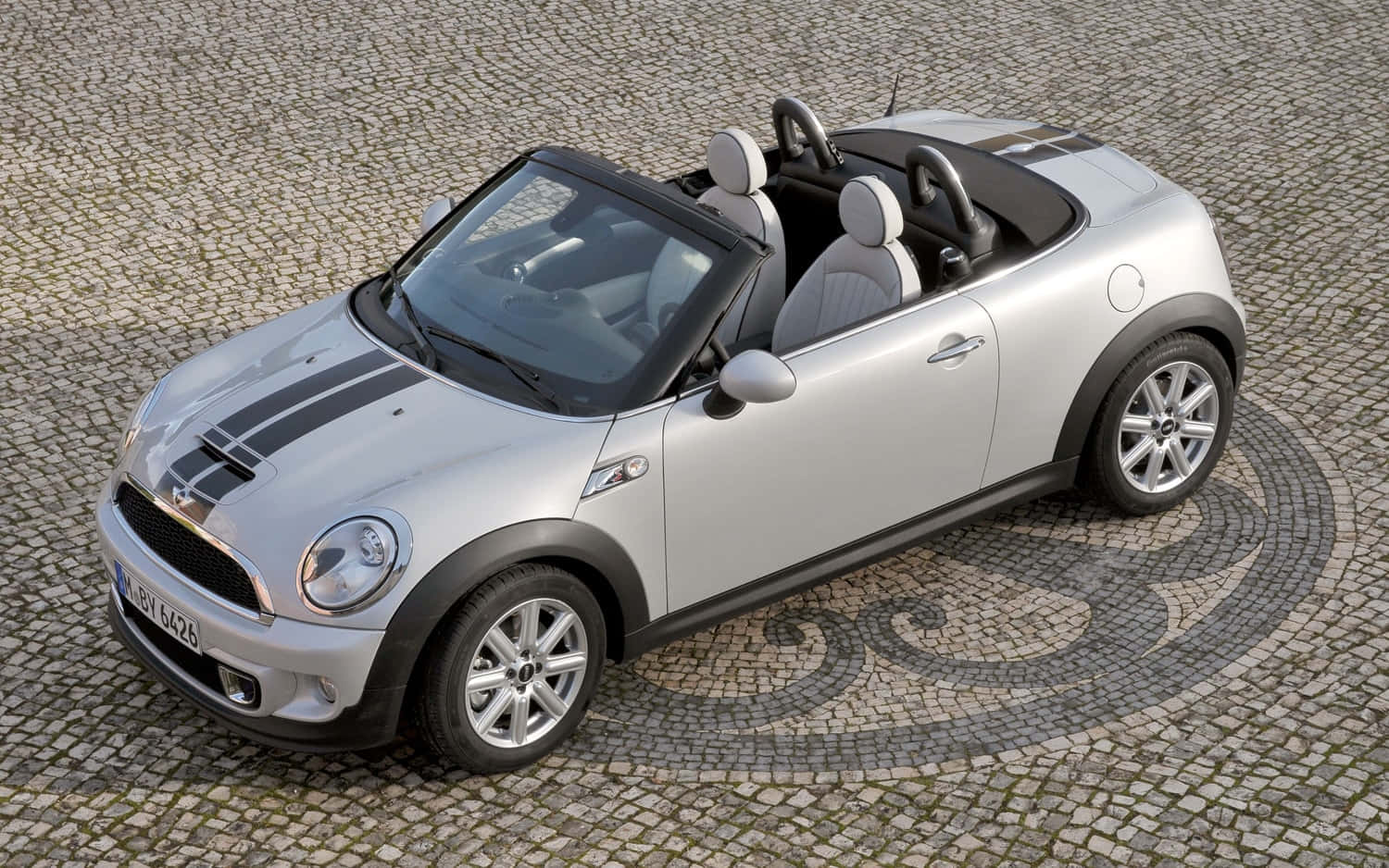  壁紙 — 一輛銀色敞篷Mini Cooper，帶有黑色賽車條紋，停在有圖案的鵝卵石廣場上。
