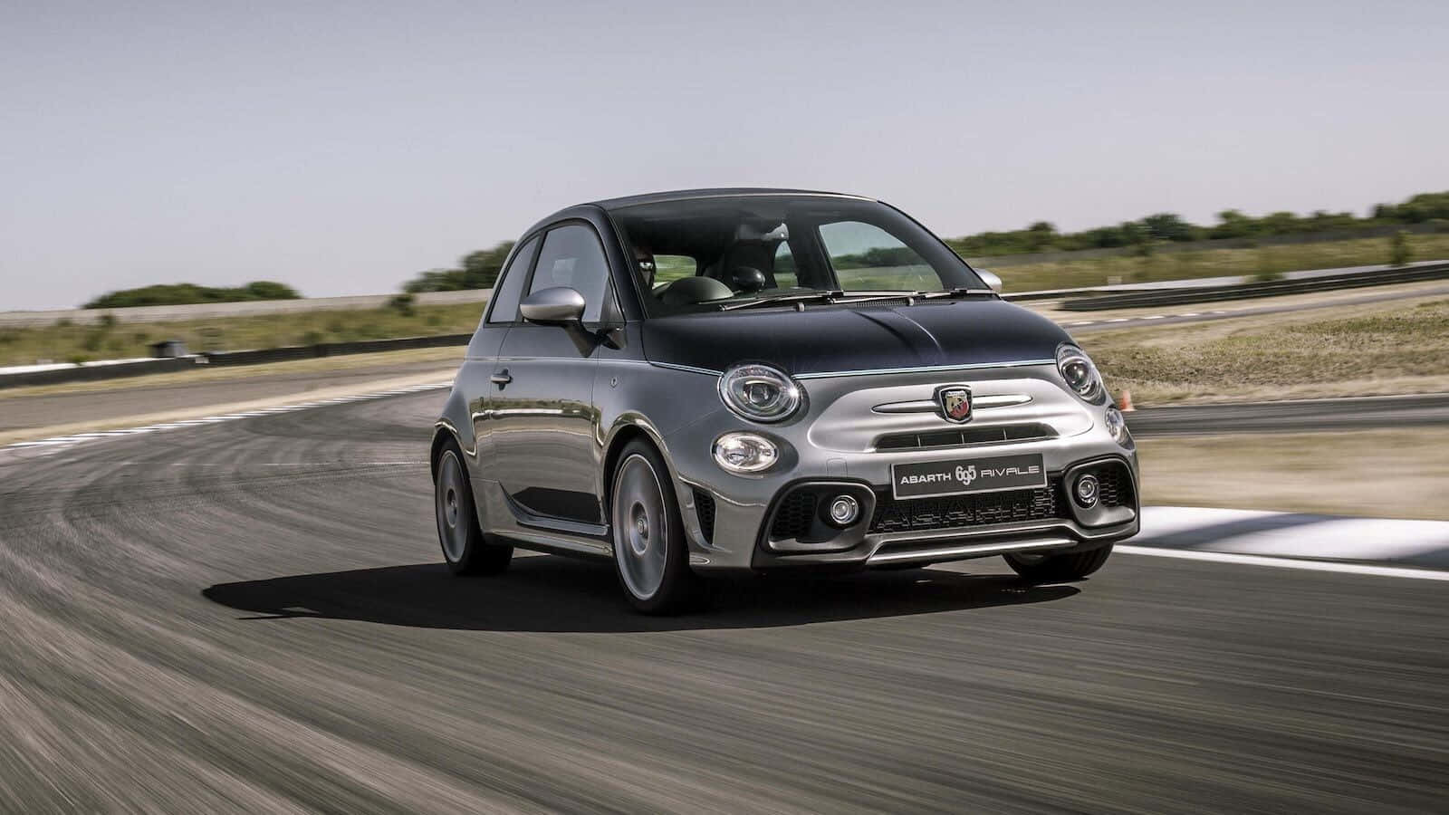 Fiat 500 桌布 壁紙 — 一輛銀色的Fiat 500 Abarth在明亮的日光下，在賽道彎道上高速奔馳，柏油路上帶有動態模糊效果。