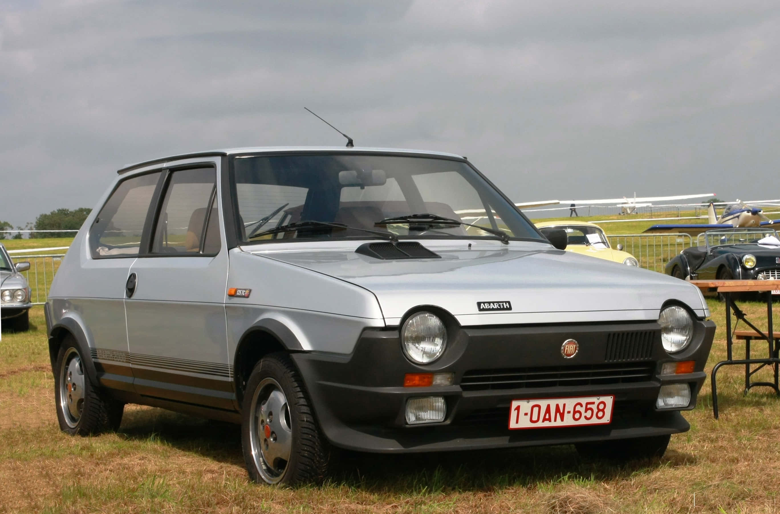 Fiat Ritmo 桌布 壁紙 — 一輛銀色的Fiat Abarth 124 Sport Spider停泊在草地的老爺車展上，天空多雲。
