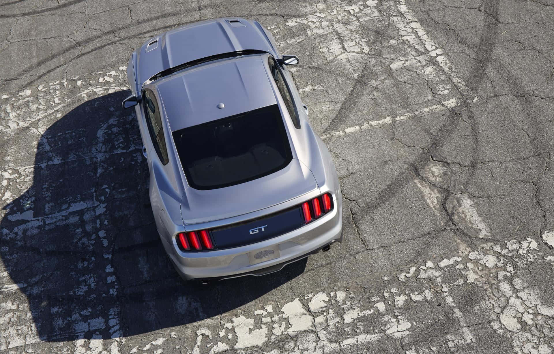 Ford Mustang California Special 桌布 壁紙 — 一輛銀色福特Mustang GT停放在裂開的柏油路上，帶有鮮明的輪胎痕跡和銳利的陰影，在明亮的陽光下。