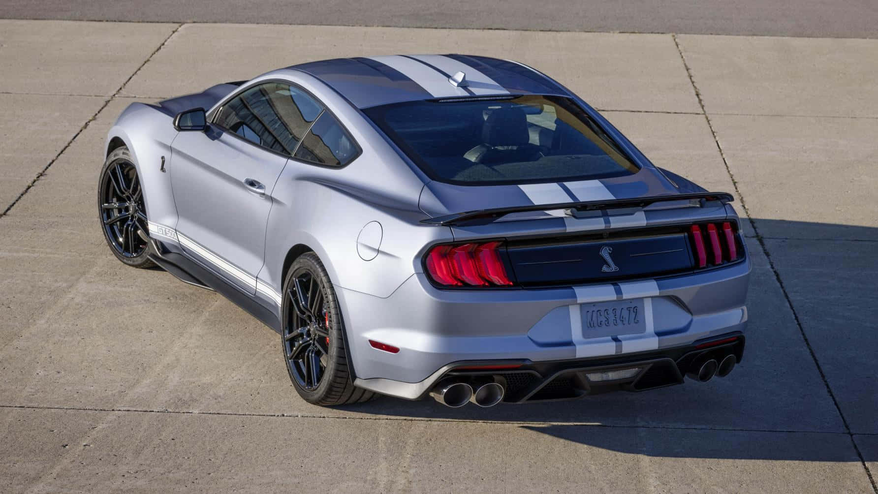  壁紙 — 一輛銀色福特Mustang Shelby GT350R，帶有黑色條紋和紅色尾燈，停在陽光燦爛的混凝土場地上。