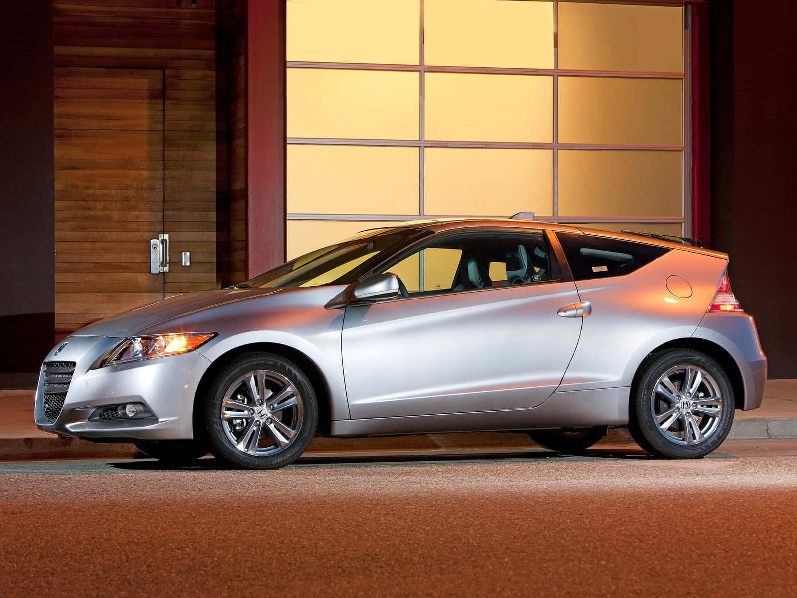 Honda Cr-z 桌布 壁紙 — 一輛時尚的銀色掀背車在夜間停在一棟現代建築前，建築物有溫暖發光的窗戶。