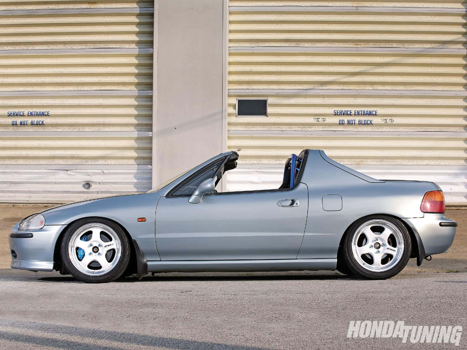 Honda Civic Del Sol 桌布 壁紙 — 一輛銀色本田S2000敞篷跑車停放在米色波紋金屬車庫門前，門上有服務入口標誌。