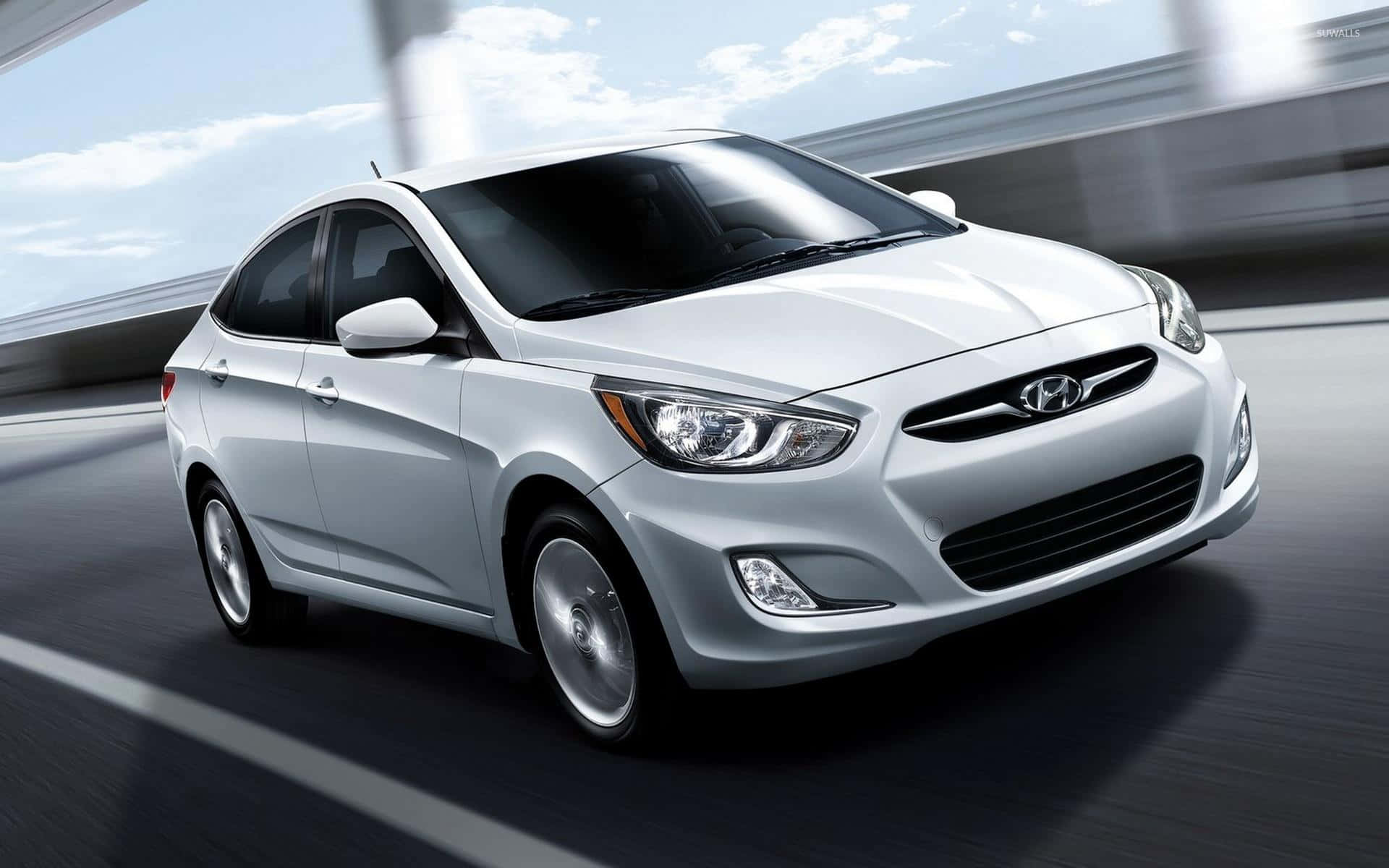 Hyundai Accent 桌布 壁紙 — 一輛時尚的銀色現代轎車在藍天白雲下高速行駛。