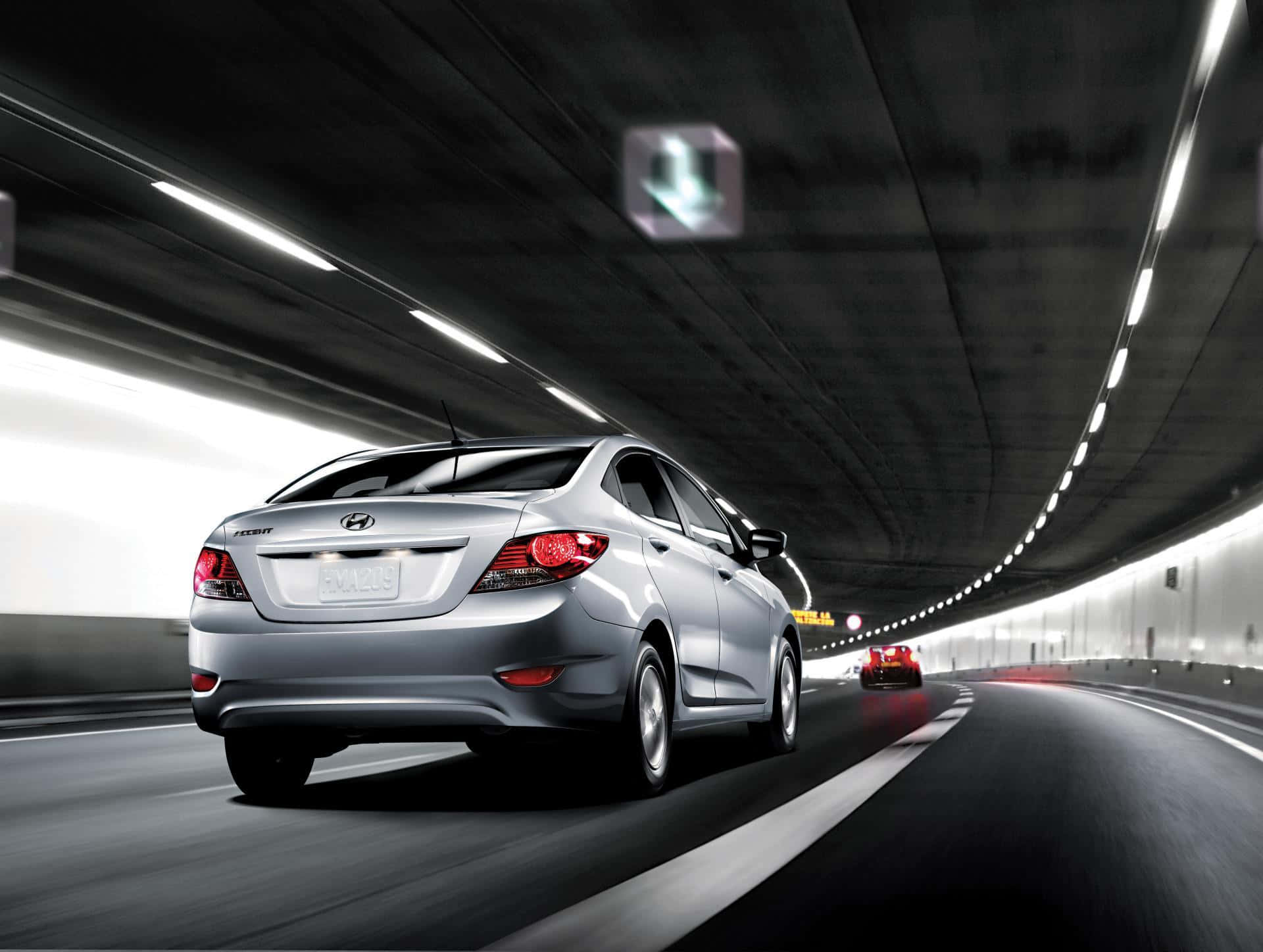 Hyundai Accent 桌布 壁紙 — 一輛銀色現代房車在昏暗的隧道中疾馳，道路上有動態模糊效果，頭頂燈光閃爍。