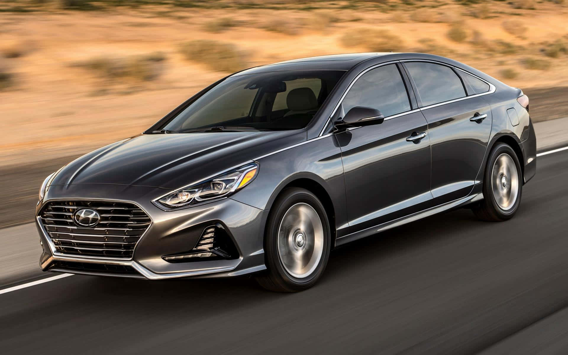 Hyundai Sonata 桌布 壁紙 — 一輛時尚的銀色現代Sonata在沙漠公路上疾馳，背景是模糊的金色地形。