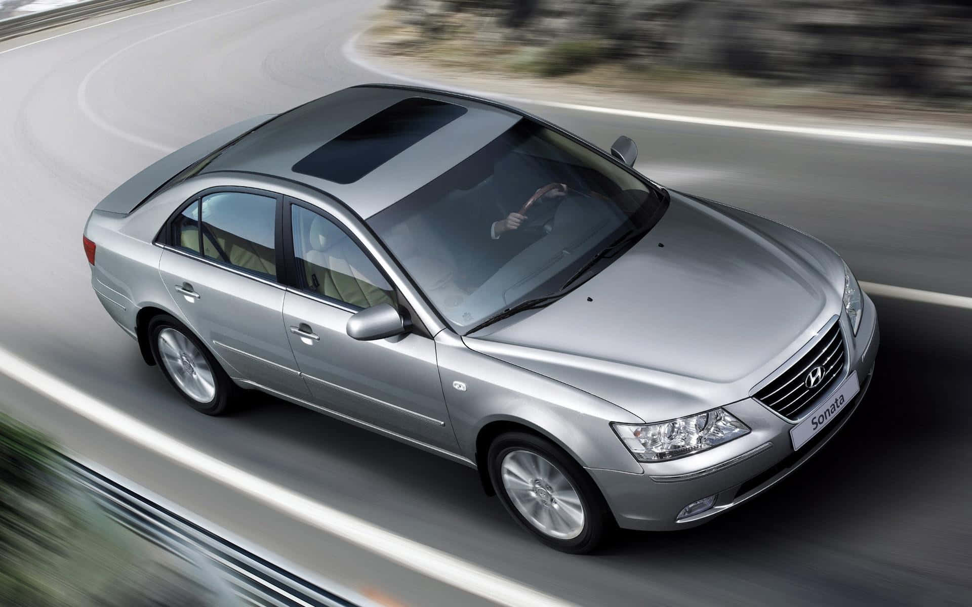 Hyundai Sonata 桌布 壁紙 — 一輛銀色現代索納塔轎車沿著彎曲的道路疾馳，動態模糊強調了其動態運動。
