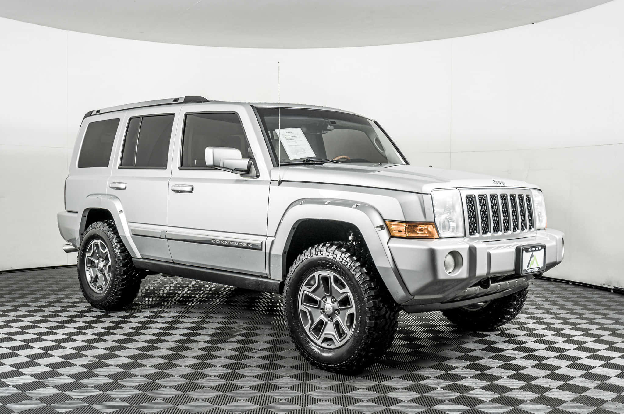 Jeep Commander 桌布 壁紙 — 一輛銀色Jeep Commander SUV配備堅固輪胎，站在明亮白色工作室的棋盤格地板上。