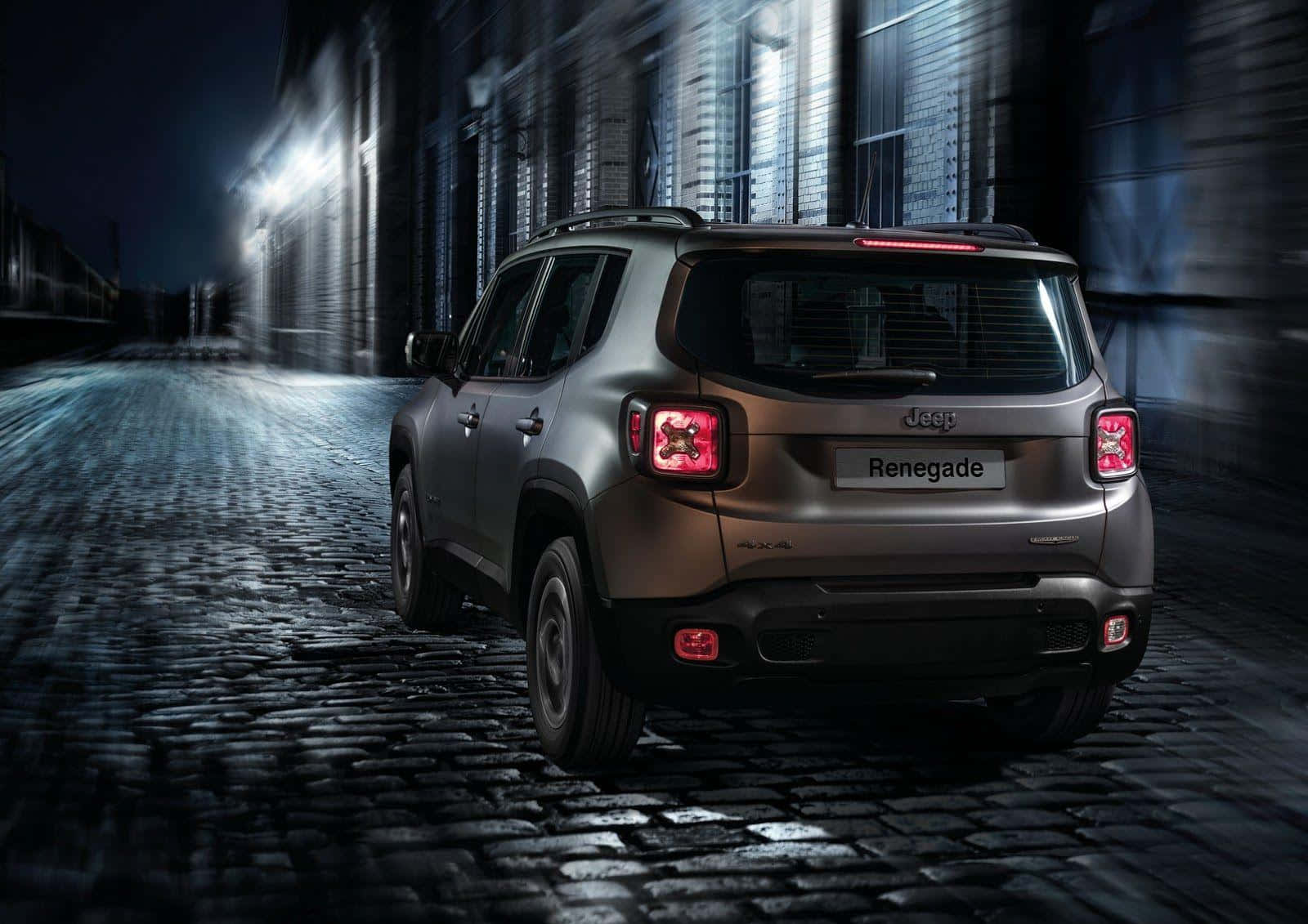 Jeep Renegade 桌布 壁紙 — 一輛銀色Jeep Renegade SUV在夜間停泊在濕漉漉的鵝卵石街道上，模糊的城市燈光掠過。