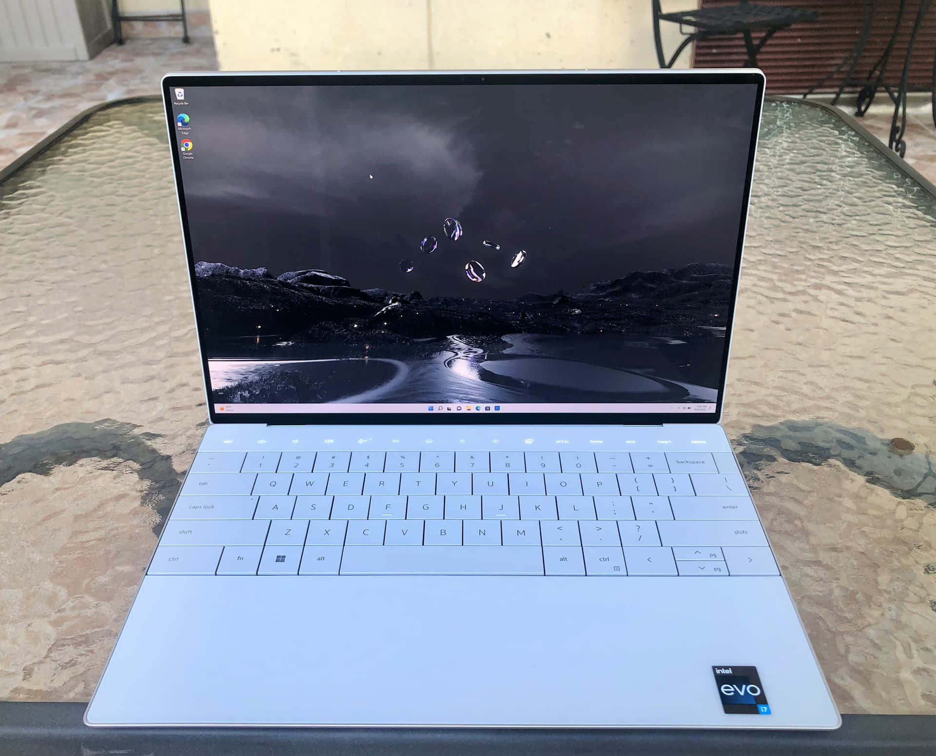 銀色筆記型電腦在玻璃桌上顯示山脈夜景桌布，帶有發光球體。 — Dell 壁紙