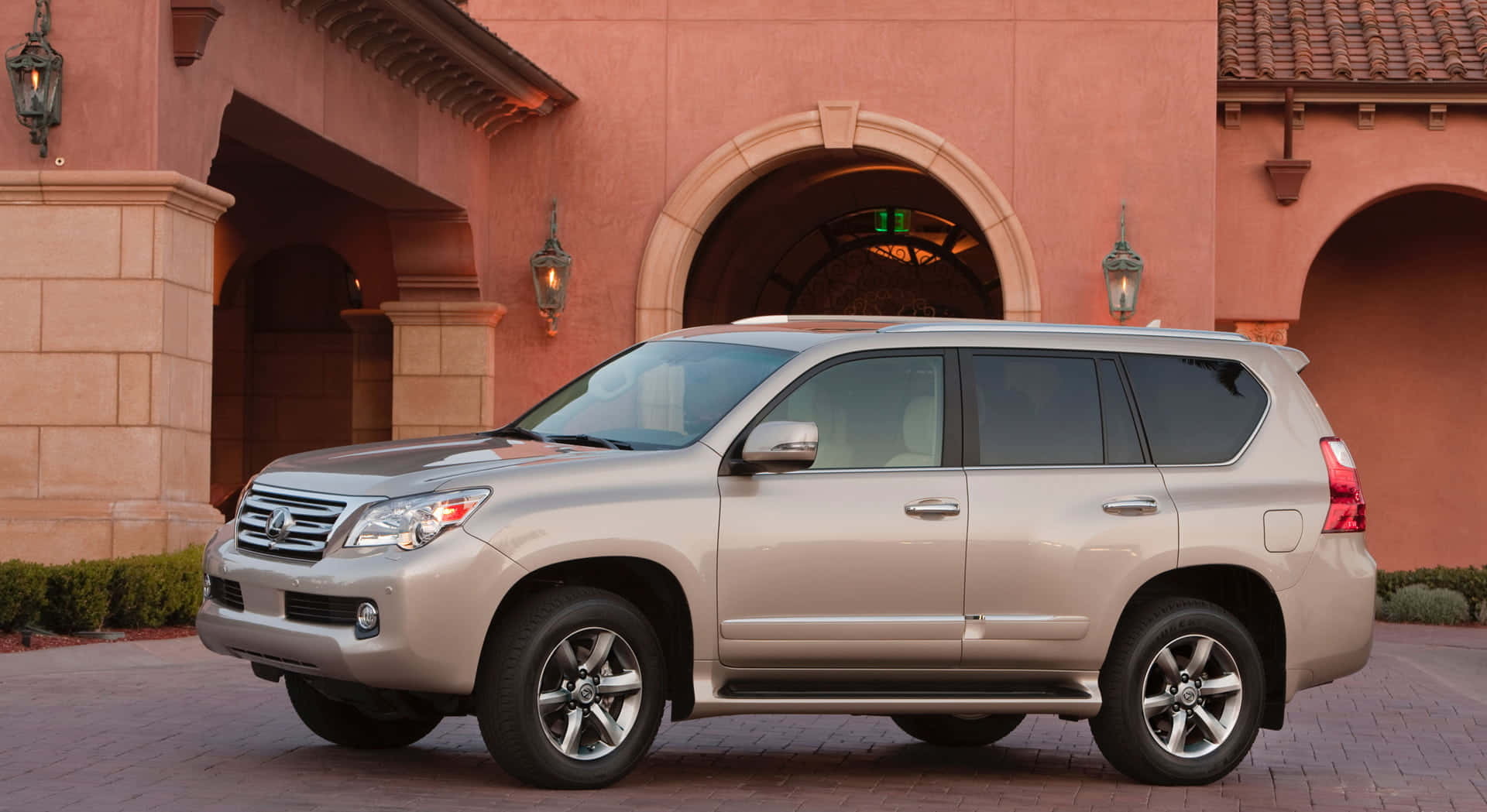 Lexus Gx 460 桌布 壁紙 — 一輛銀色Lexus GX SUV停放在磚砌車道上，前方是帶有拱門的陶土色西班牙風格建築。