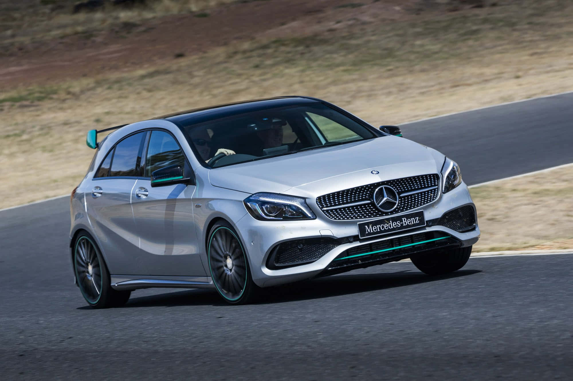 Mercedes Benz A-class 桌布 壁紙 — 一輛銀色 Mercedes-Benz A45 AMG 在蜿蜒的柏油路上疾馳，背景是乾燥的草坡。