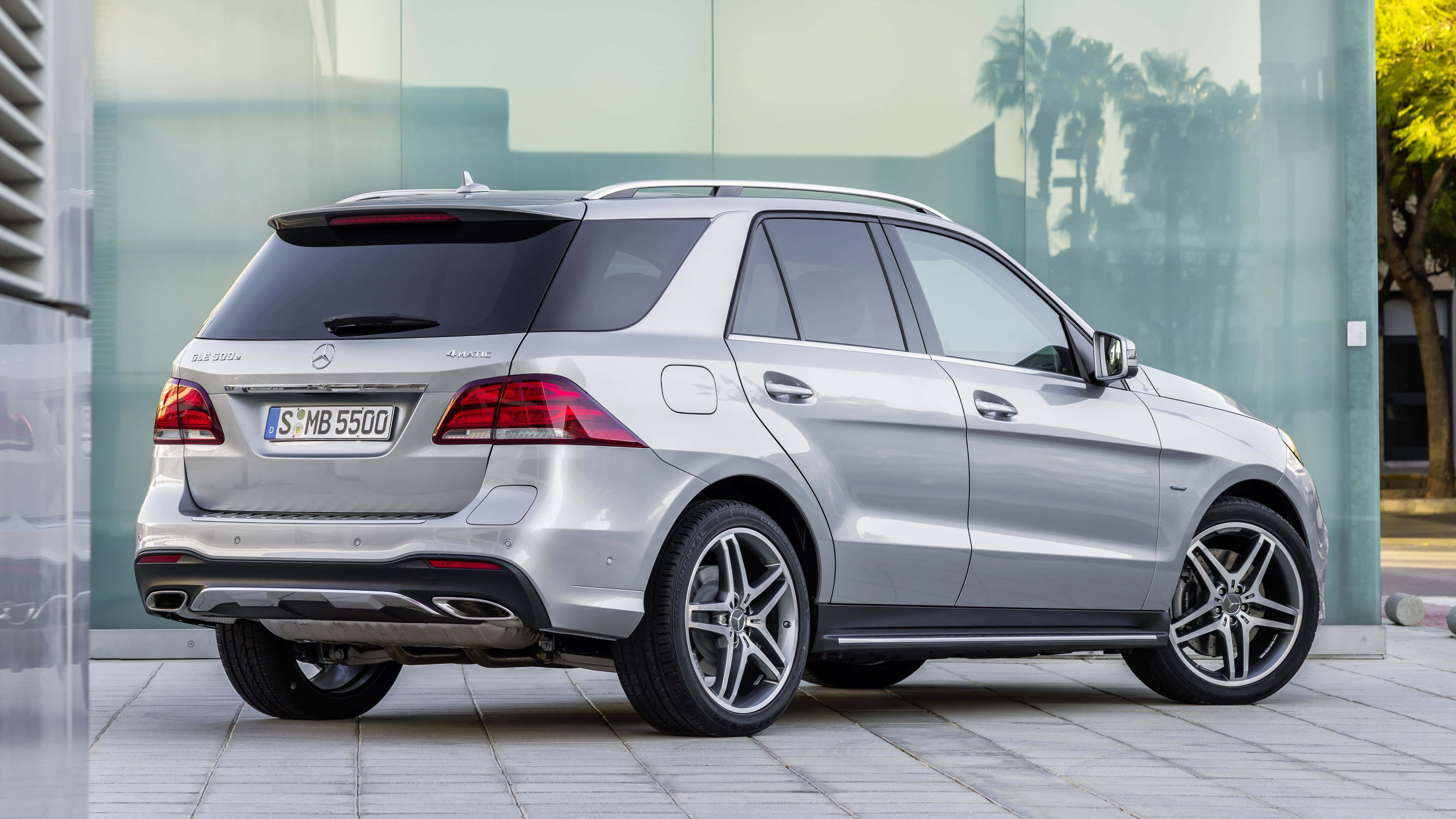 Mercedes Benz Gle-class 桌布 壁紙 — 一輛時尚的銀色 Mercedes-Benz GLE SUV 停放在磁磚鋪設的人行道上，旁邊是一座玻璃建築，窗戶反射出棕櫚樹。