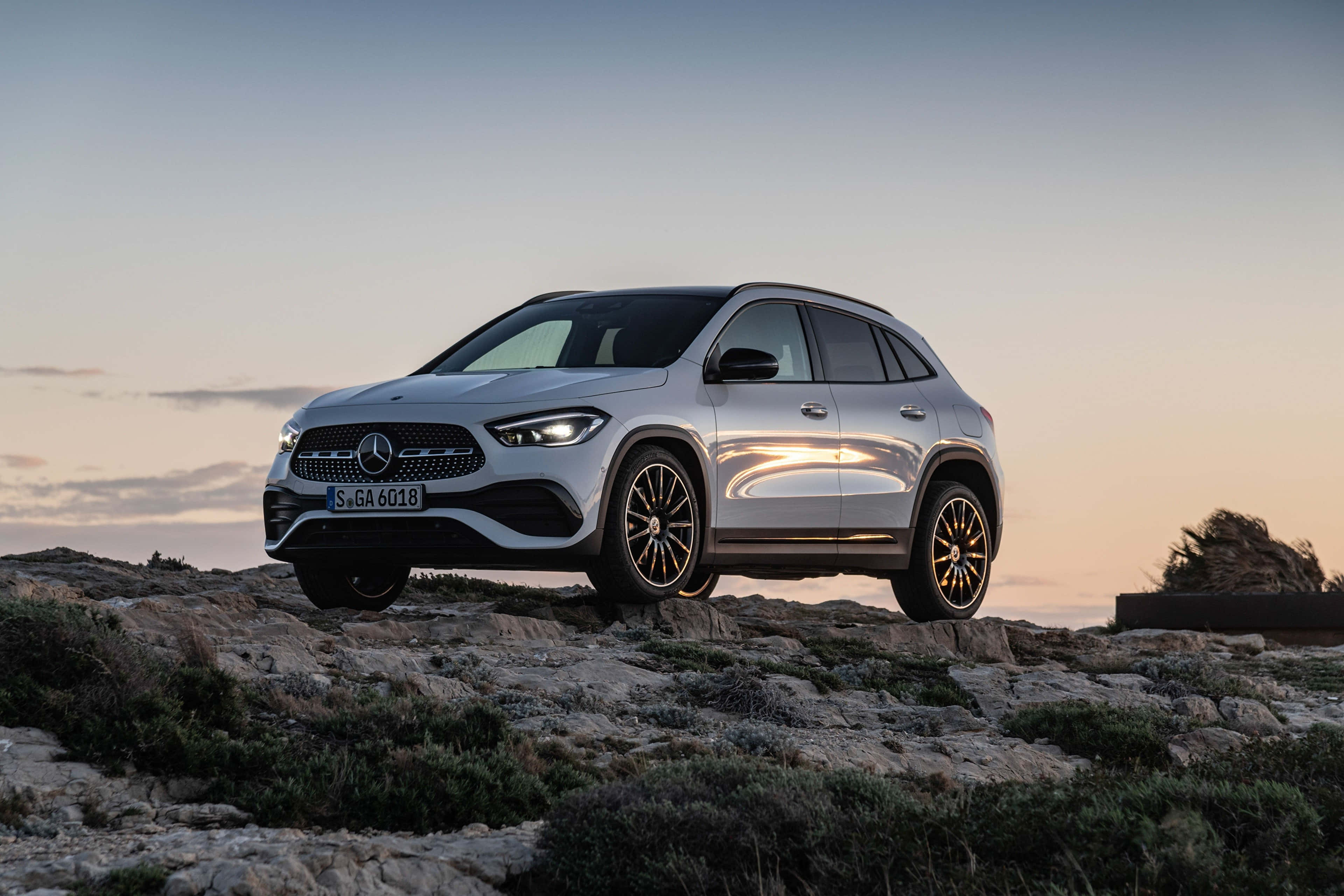 Mercedes Benz Gla-class 桌布 壁紙 — 一輛時尚的銀色Mercedes-Benz SUV在日落時分停泊在岩石懸崖上，溫暖的金色光線反射在其拋光表面上。