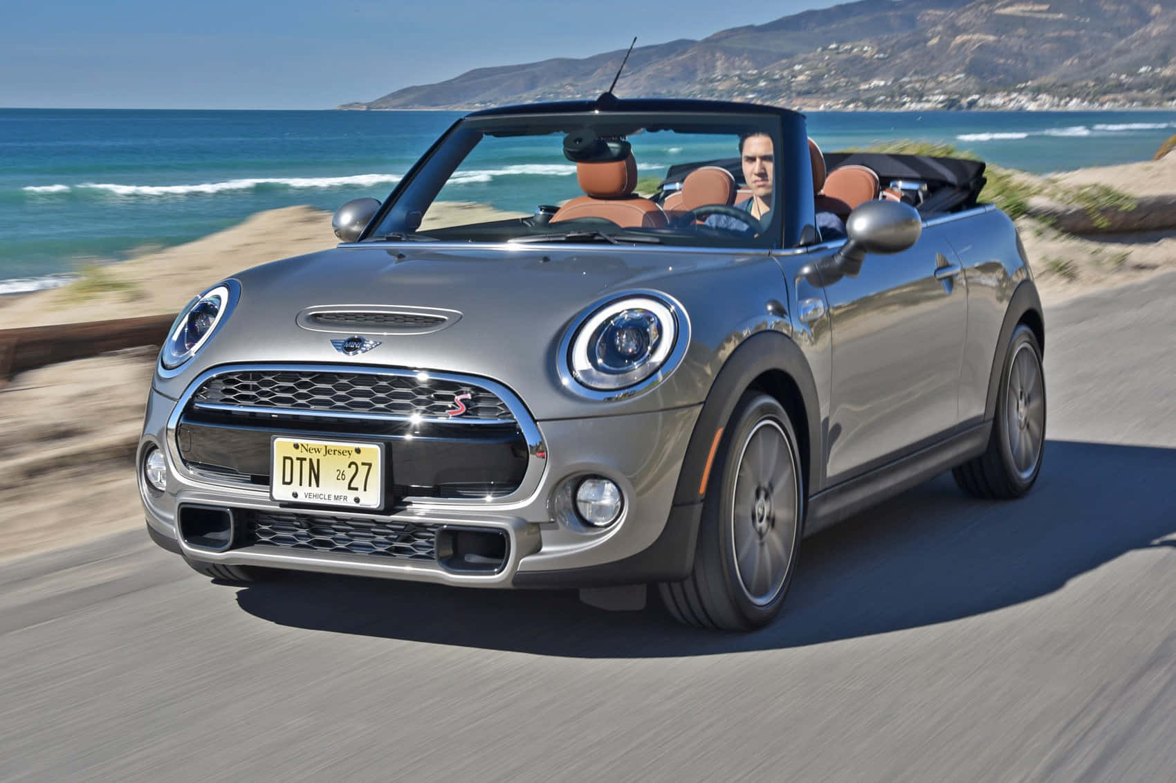 Mini Cooper Convertible 桌布 壁紙 — 一輛銀色MINI Cooper敞篷車沿著海岸公路疾駛，背景有海浪和山脈。