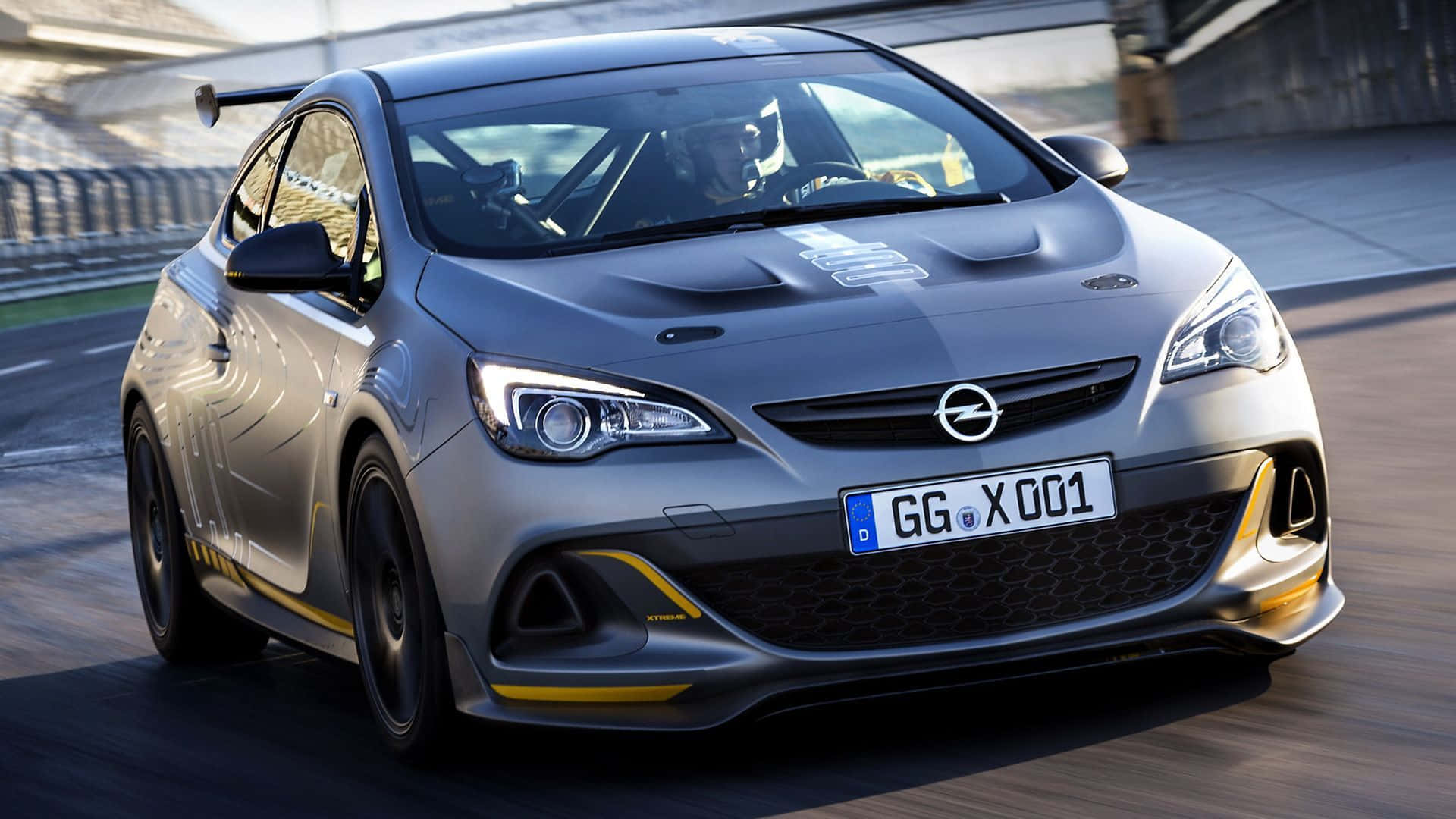 Opel Astra 桌布 壁紙 — 一輛銀色歐寶雅特GTC賽車在賽道上飛馳，帶有黃色點綴，車內駕駛清晰可見。