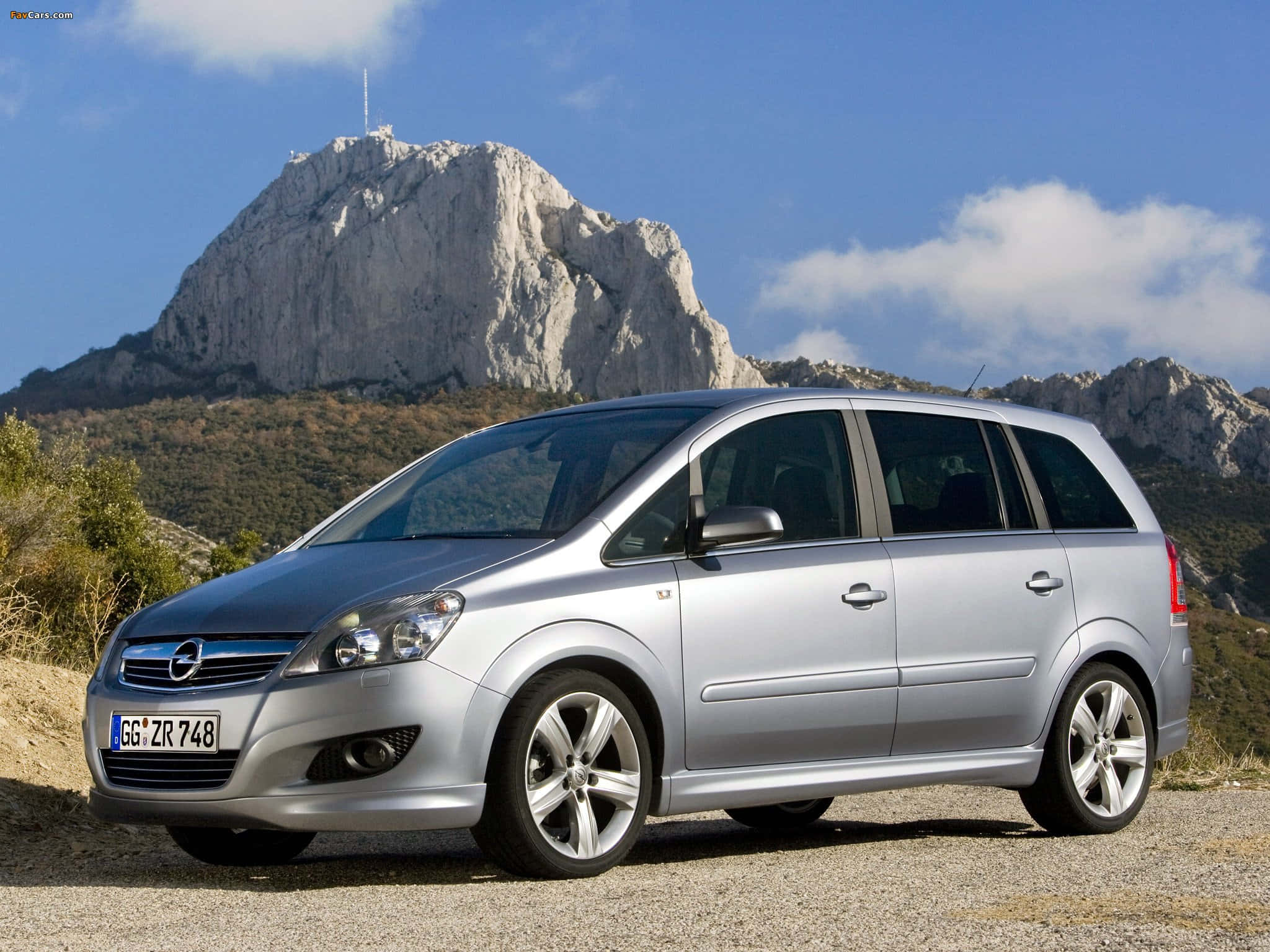 Opel Zafira 桌布 壁紙 — 一輛銀色歐寶Zafira停泊在碎石上，背後有一座巨大的岩石山在明亮的藍天下聳立。