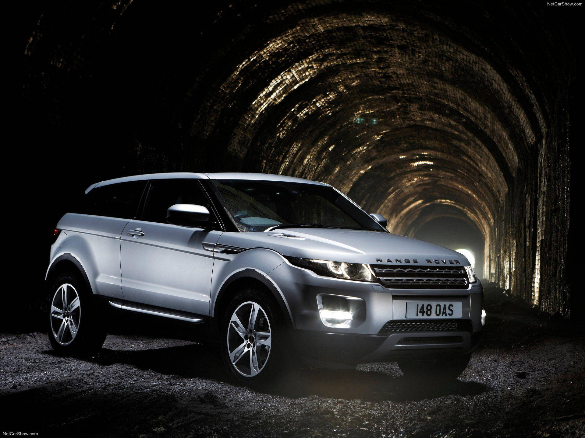 銀色 Range Rover Evoque 停在黑暗的石隧道中，車頭燈亮著。 — 4K 壁紙