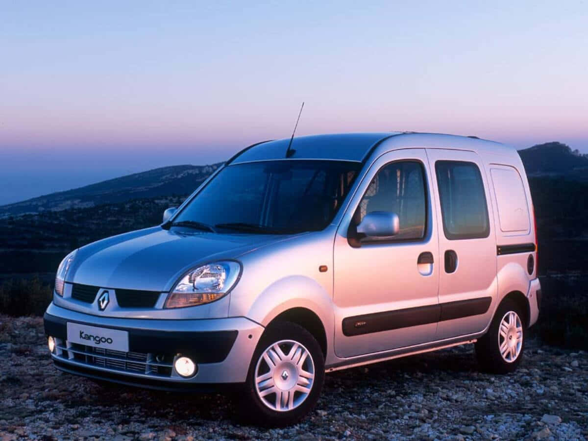 Renault Kangoo 桌布 壁紙 — 一輛銀色雷諾Kangoo廂型車停泊在岩石山坡上，暮色中背後是柔和的紫色和藍色天空。