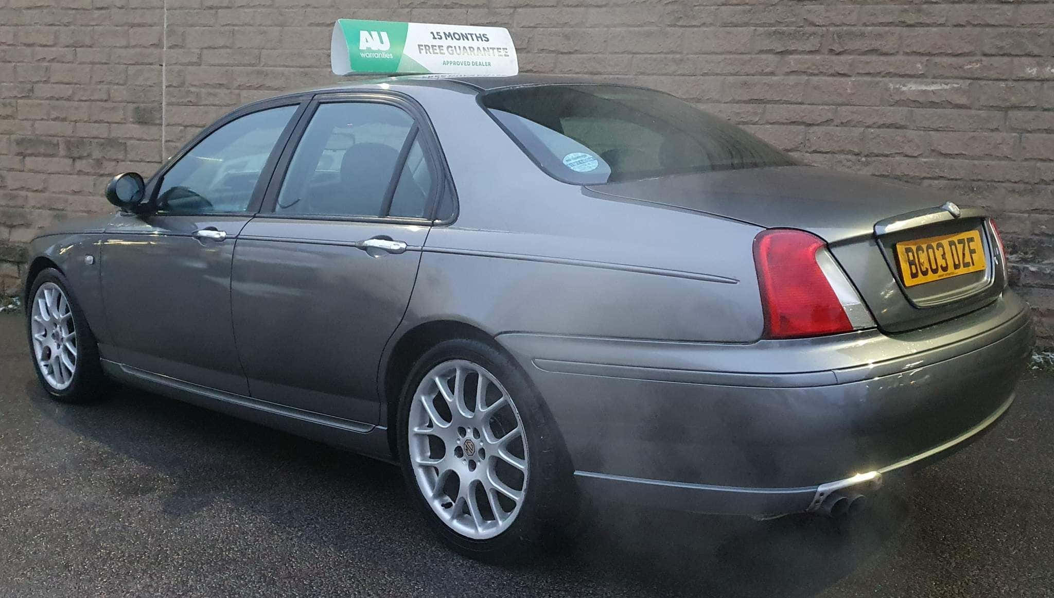 Mg Zt 桌布 壁紙 — 一輛帶有AU品牌和15個月保修標誌的銀色計程車停在磚牆旁，排放著廢氣煙霧。