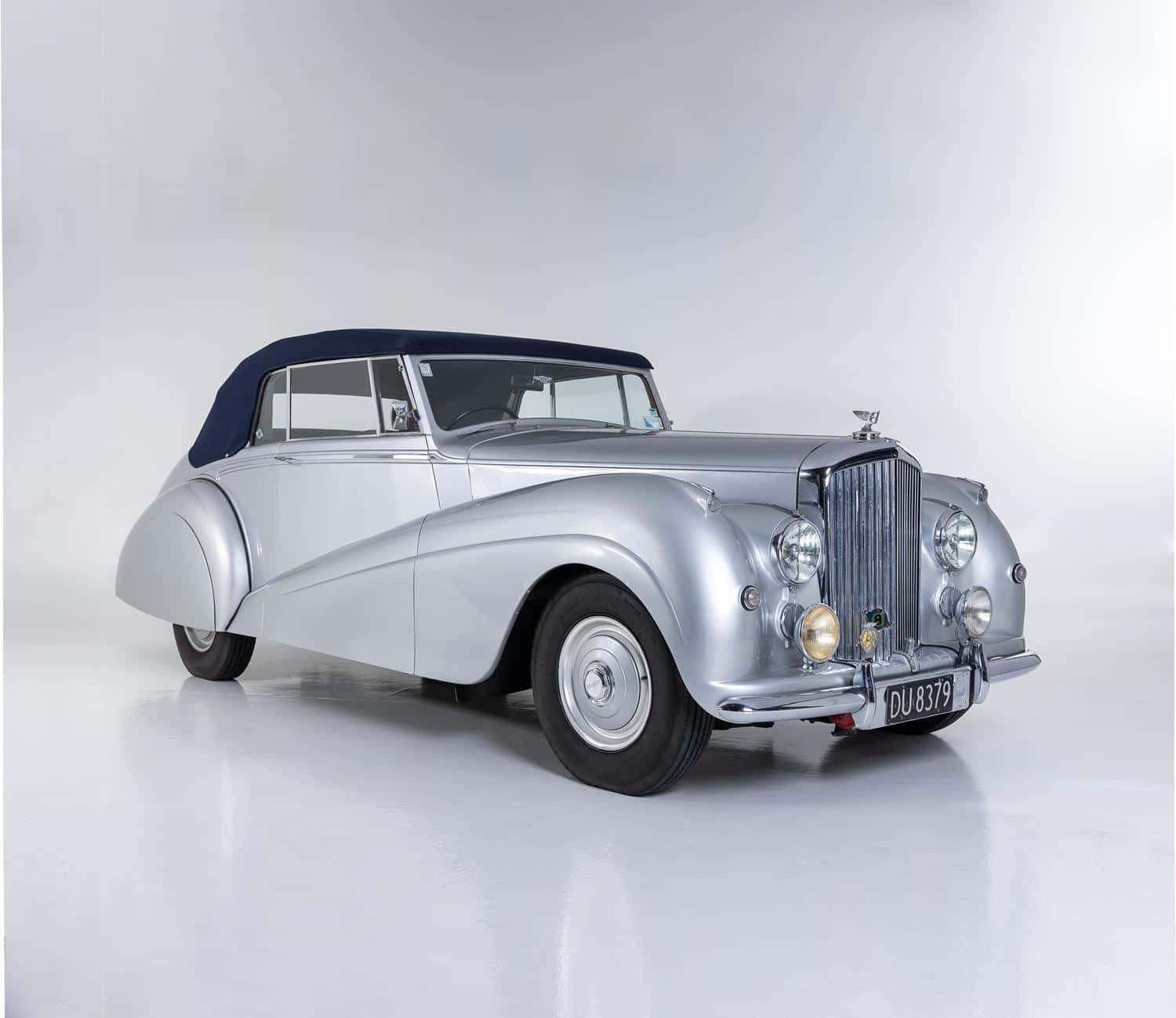 Bentley Mark Vi 桌布 壁紙 — 一架時尚的銀色復古敞篷車，配海軍藍軟頂，在簡約的白色工作室背景前蓄勢待發。