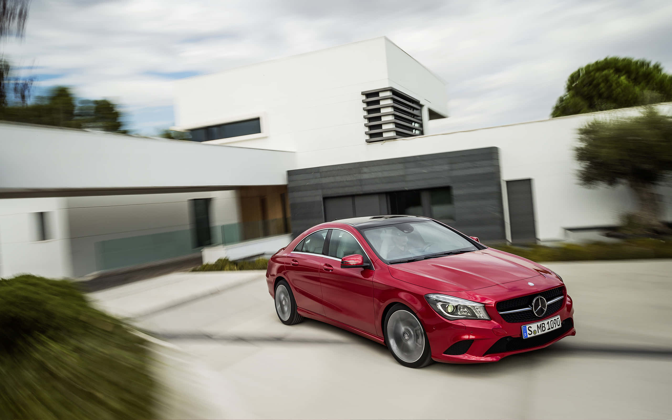 Mercedes Benz Cla-class 桌布 壁紙 — 一輛鮮紅色的 Mercedes-Benz CLA 轎車以動態模糊效果駛過一棟現代白色房屋。