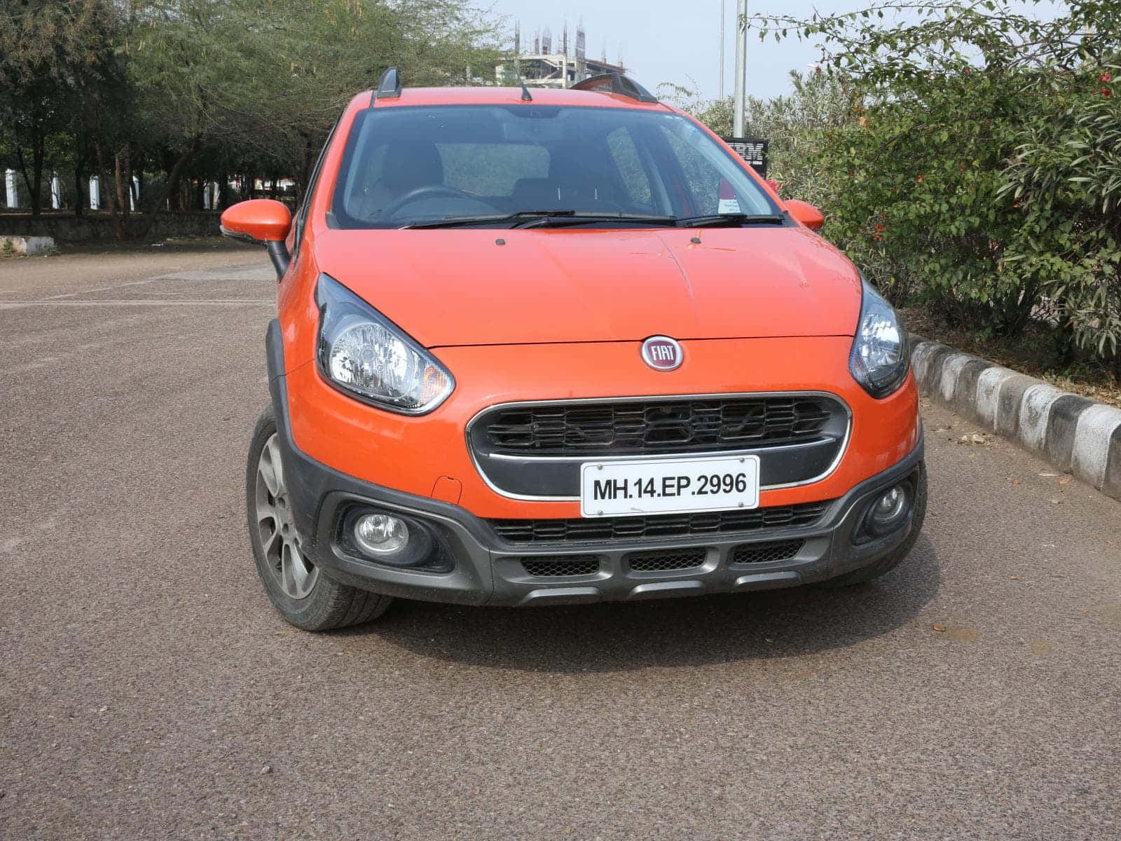 Fiat 500l 桌布 壁紙 — 鮮豔的橙色 Fiat Panda 停在瀝青路上，背景有綠樹和條紋路緣。
