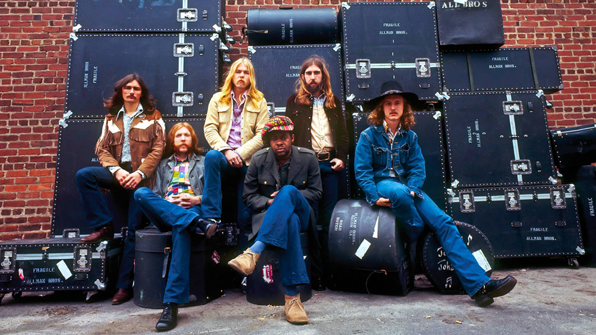 音樂 桌布 壁紙 — Allman Brothers Band 的六位成員隨意地靠在磚牆上，周圍環繞著他們的黑色設備箱。