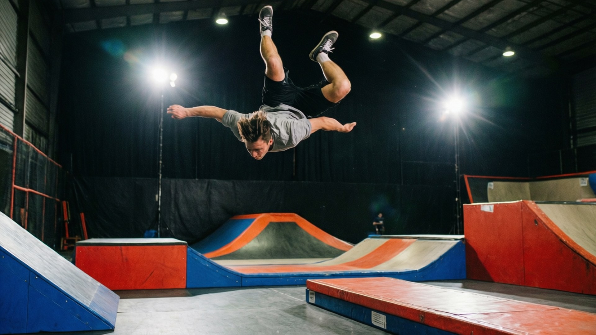 Mid-Air Flip 壁紙 — 一名滑板手在室內滑板場的明亮聚光燈下，於色彩繽紛的坡道上空進行翻轉動作。