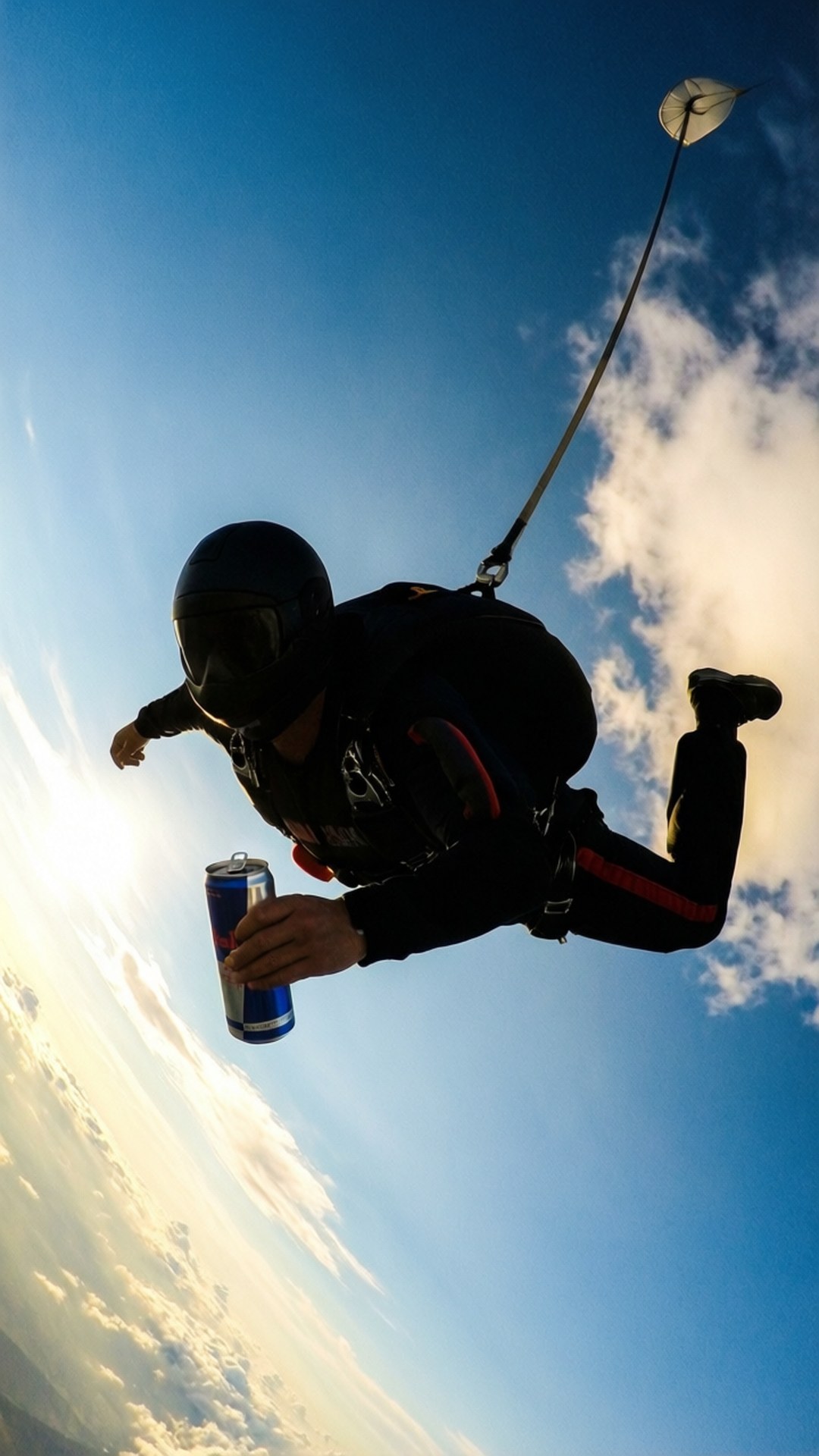 Skydive with Red Bull 壁紙 — 一名跳傘運動員的剪影在自由落體時手持紅牛罐，背景是明亮的藍天和散落的雲朵。