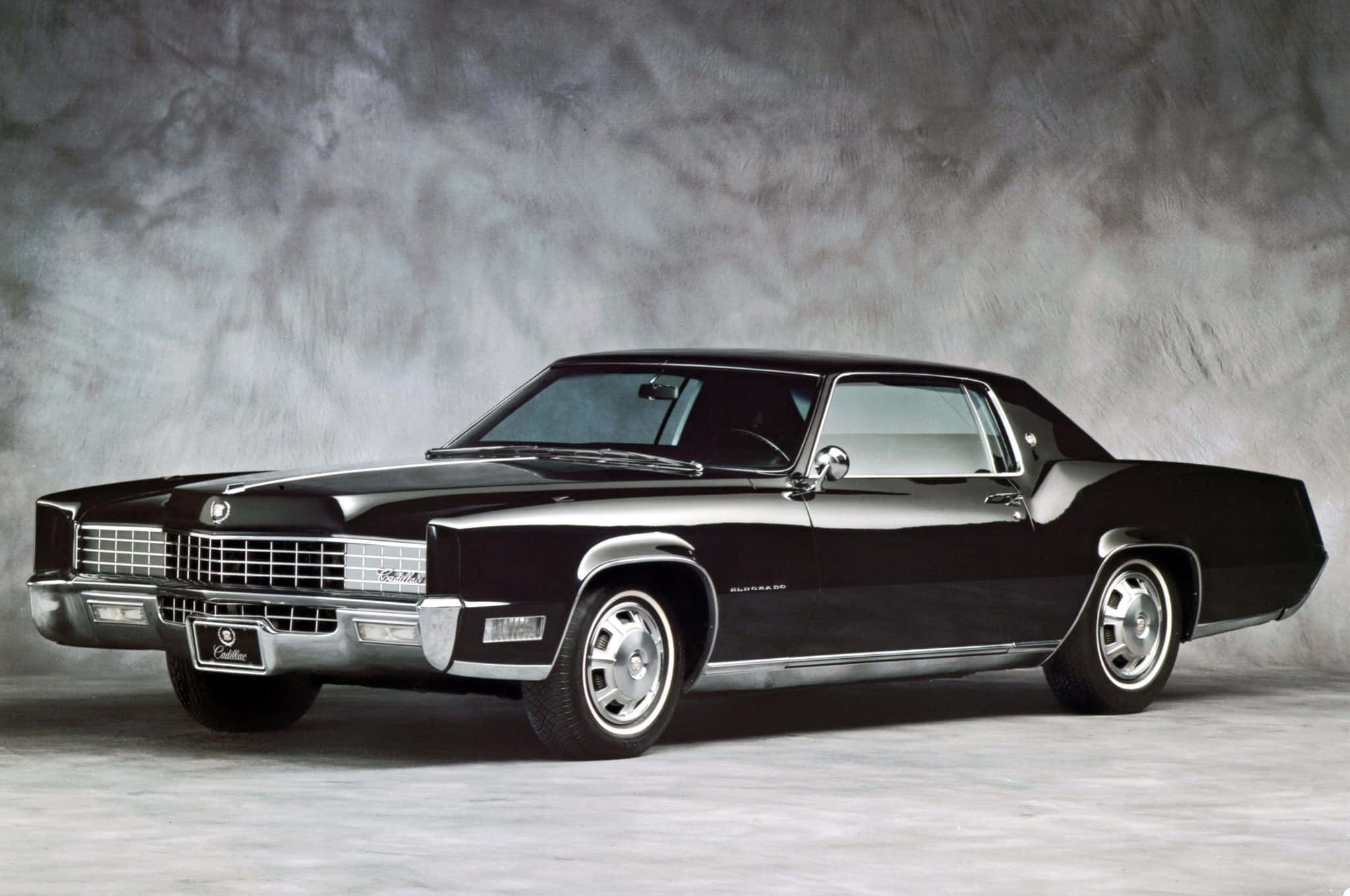 Cadillac Fleetwood 桌布 壁紙 — 一輛光滑的黑色1970年代凱迪拉克Coupe DeVille在攝影棚燈光下閃閃發光，背景是帶紋理的灰色。
