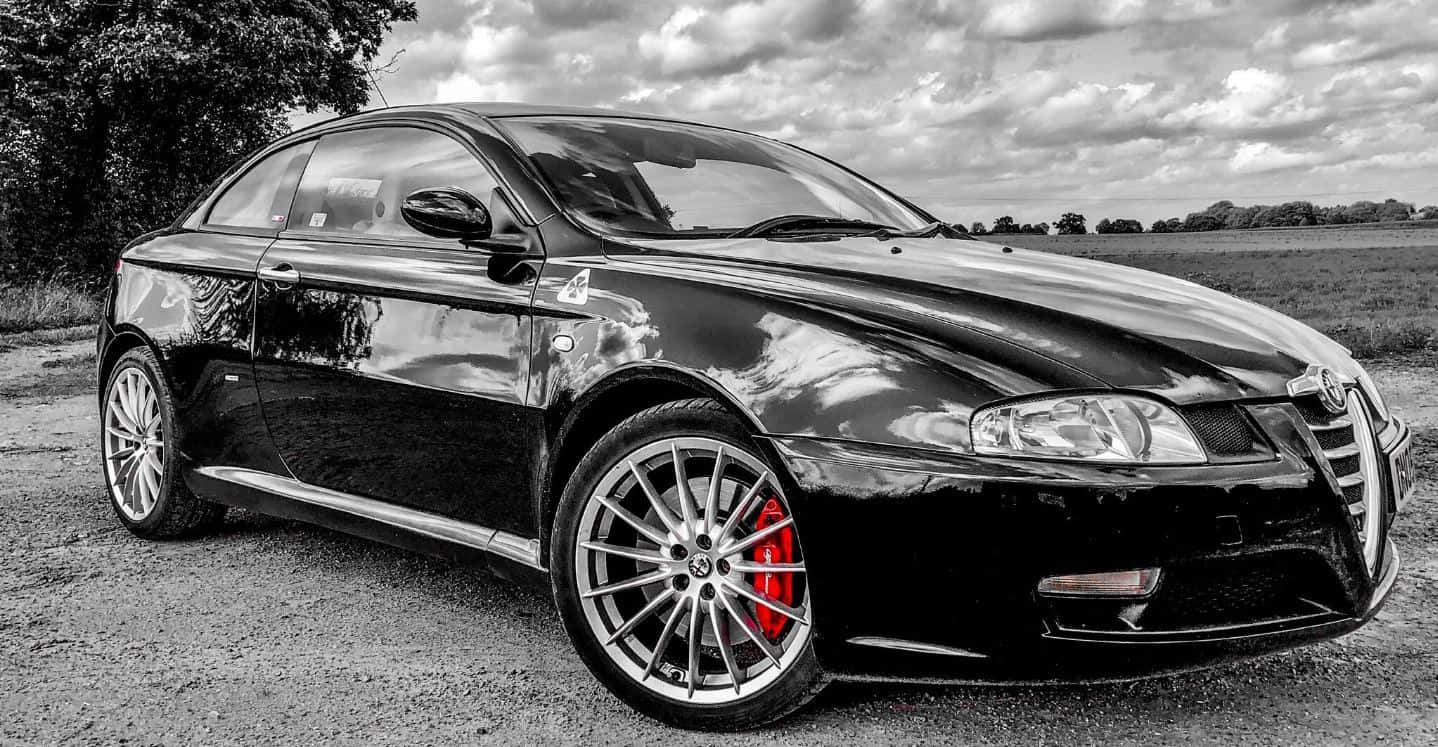 Alfa Romeo Gt 桌布 壁紙 — 一輛時尚的黑色阿爾法羅密歐跑車，帶有紅色制動卡鉗，停在多雲天空下的碎石路上。