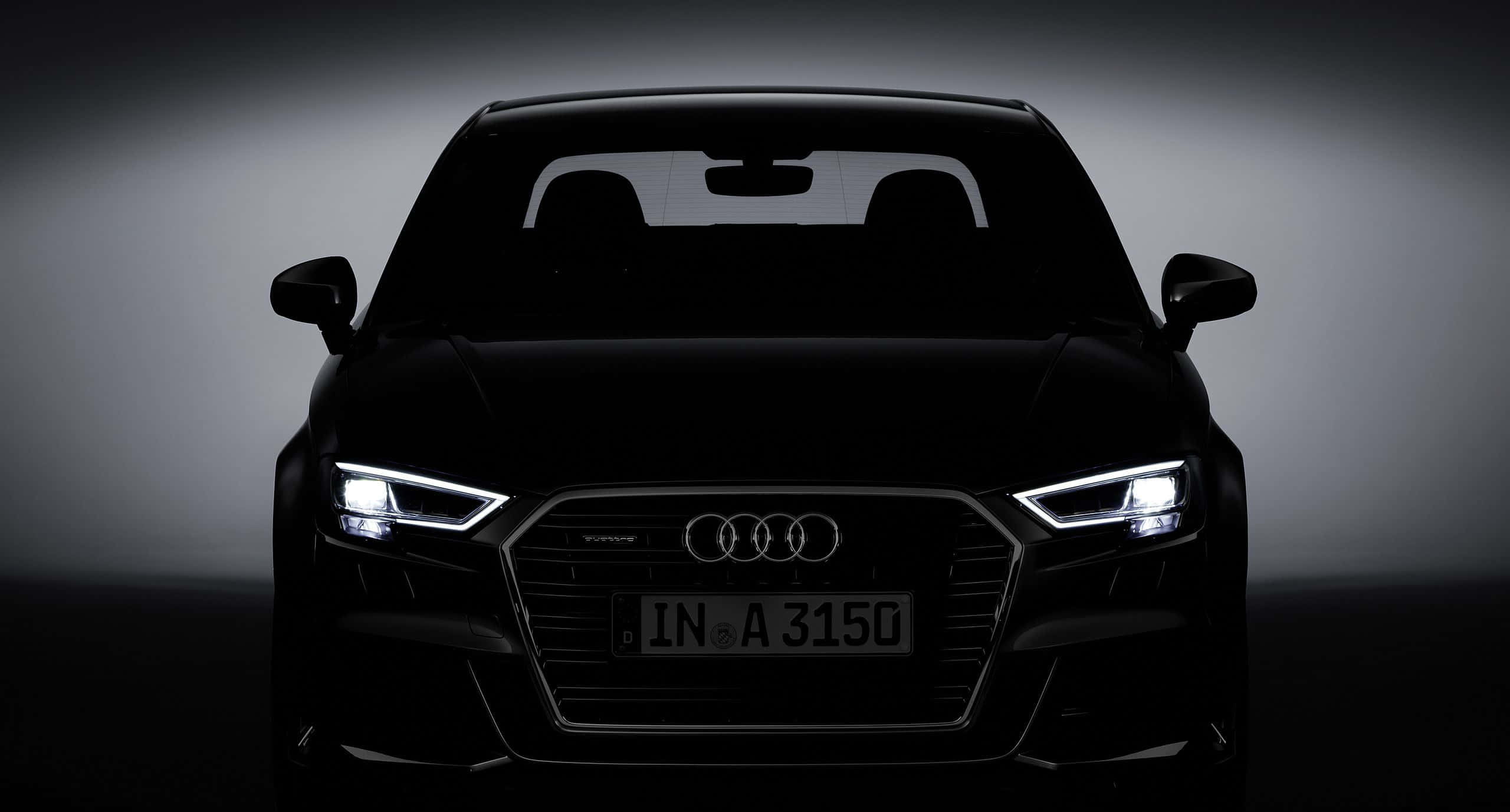 Audi A3 桌布 壁紙 — 一輛時尚的黑色奧迪汽車輪廓，在深色漸變工作室背景下被發光的車頭燈照亮。