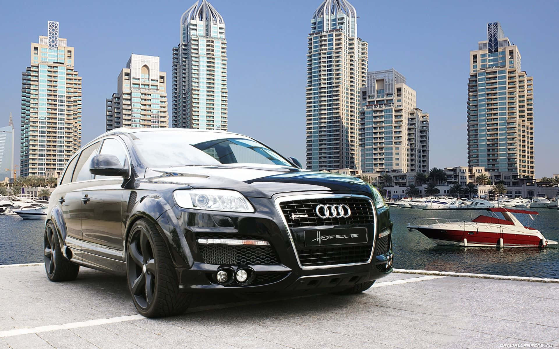 Audi Q7 桌布 壁紙 — 一架時尚的黑色奧迪Q7跑車停在海濱碼頭上，背景是豪華遊艇和高聳的摩天大樓，天空湛藍。