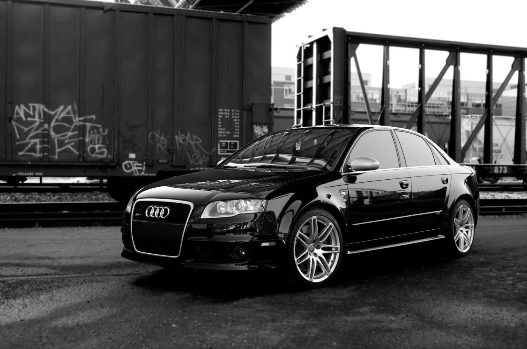 Audi Rs5 桌布 壁紙 — 一輛時尚的黑色奧迪轎車配備定制輪圈，停在工業橋下塗鴉覆蓋的火車車廂旁。
