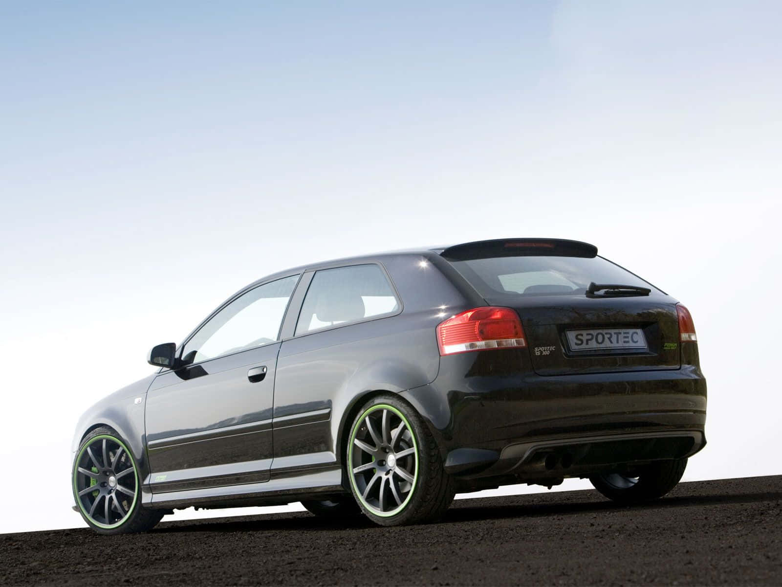 Audi S3 桌布 壁紙 — 一輛時尚的黑色Audi Sportec掀背車，帶有發光的綠色輪圈，停在晴朗天空下的深色碎石上。