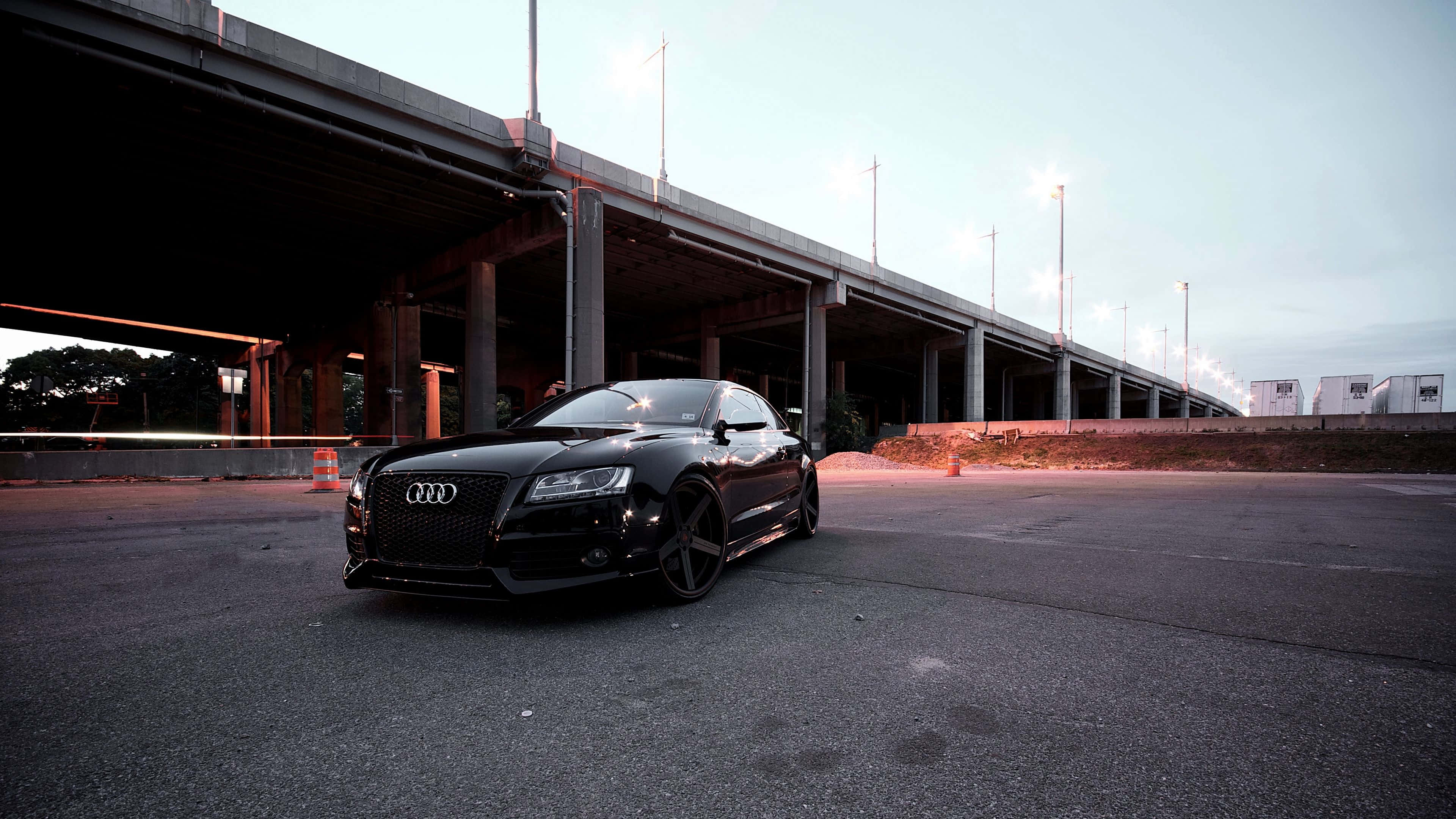 Audi A4 桌布 壁紙 — 一輛時尚的黑色奧迪跑車停放在混凝土天橋下，暮色中街燈閃爍。