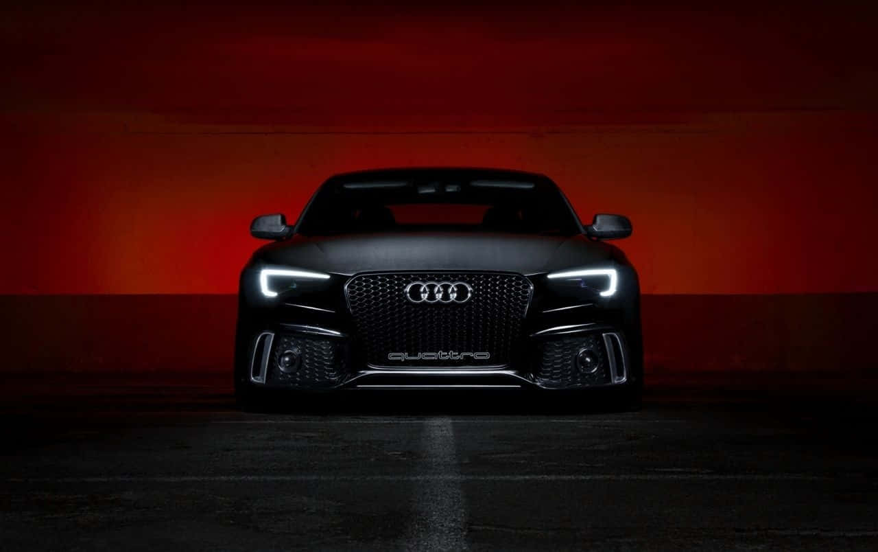 Audi S5 桌布 壁紙 — 一輛時尚的黑色奧迪跑車，車頭燈閃爍，在昏暗的攝影棚中，面向戲劇性的紅橙色漸變牆凝視前方。