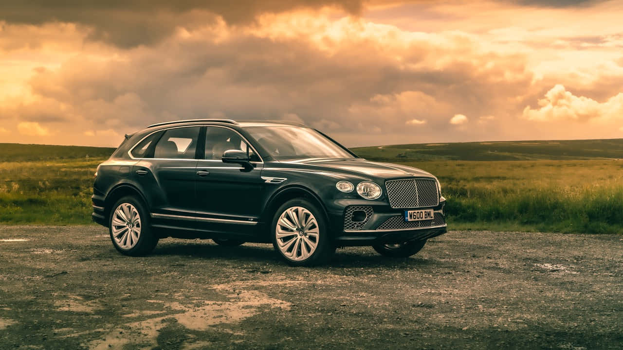 Bentley Bentayga 桌布 壁紙 — 一輛時尚黑色賓利Bentayga SUV停泊在碎石路上，背景是戲劇性的金色日落天空。