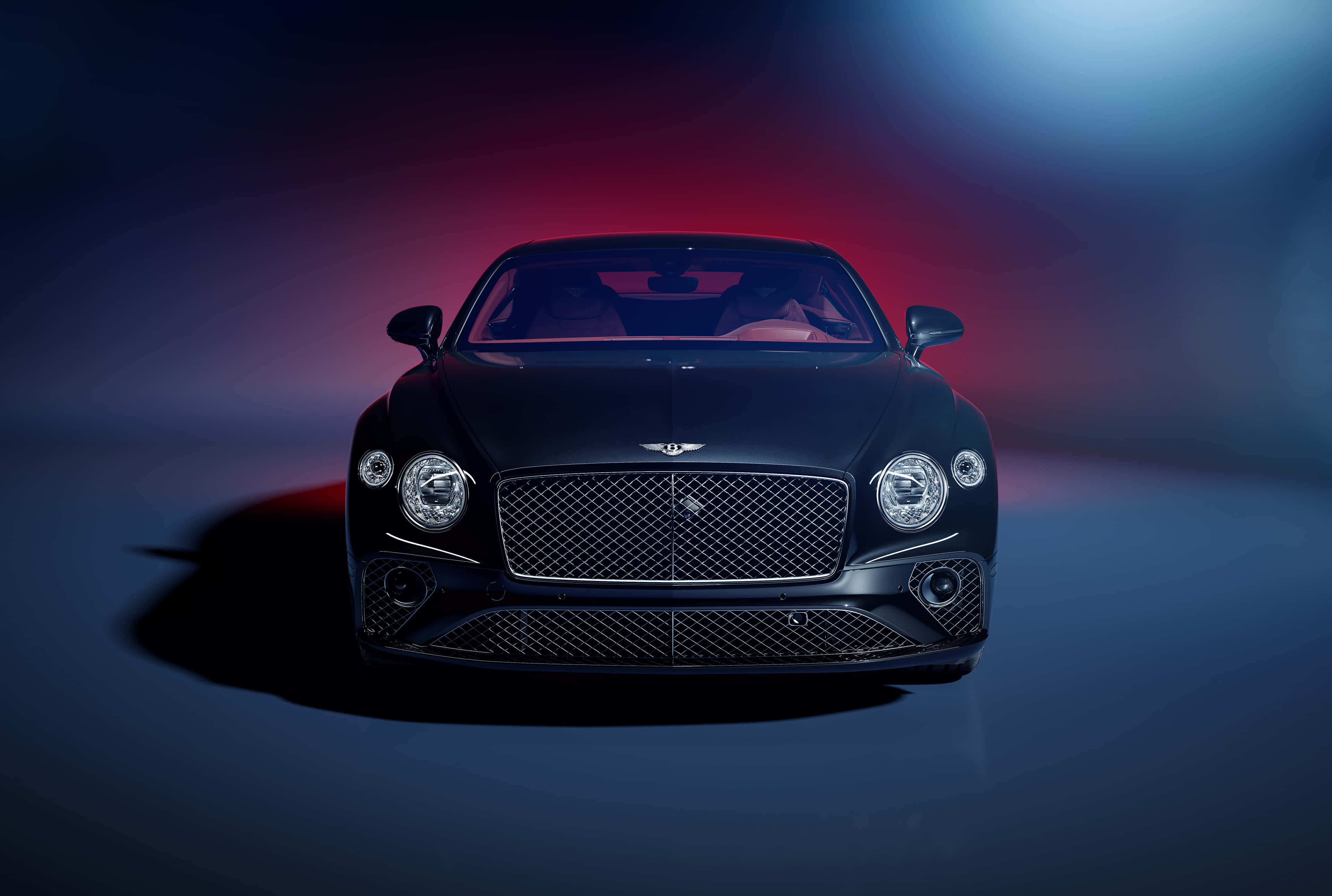 Bentley Continental Gt 桌布 壁紙 — 一輛時尚的黑色賓利 Continental GT 在戲劇性的紅藍工作室燈光下正面朝前，投射出大膽的陰影。