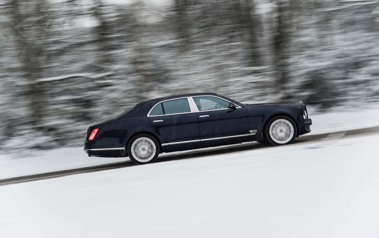 Bentley Mulsanne 桌布 壁紙 — 一輛時尚的黑色賓利 Mulsanne 在雪地森林中疾馳，背景是模糊的冬季樹木。