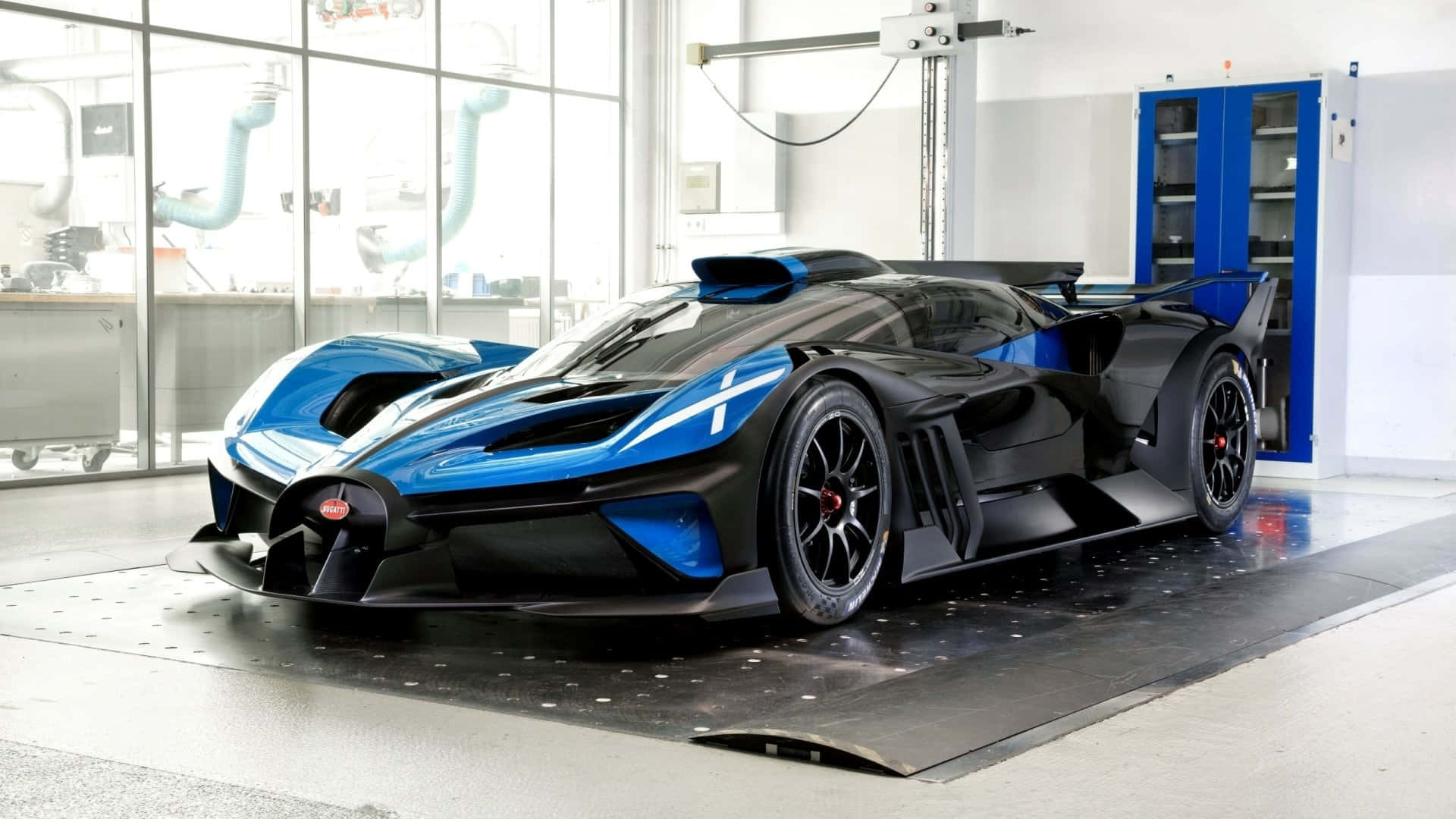 Bugatti Bolide 桌布 壁紙 — 一輛時尚的黑色和藍色布加迪超跑，採用空氣動力學設計，停在明亮現代車庫的升降機上。