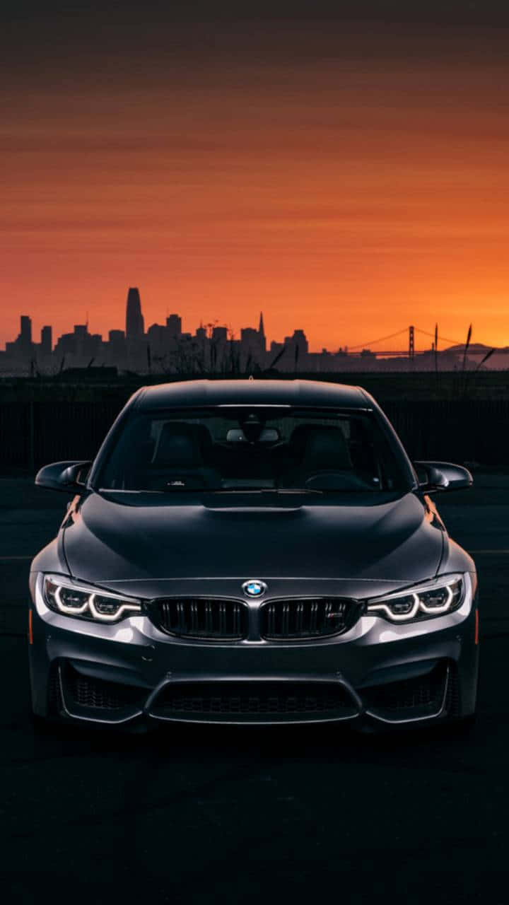 Sunset Drive 桌布 壁紙 — 一輛時尚的黑色BMW M4在火熱的橙色日落和城市天際線剪影下向前行駛。