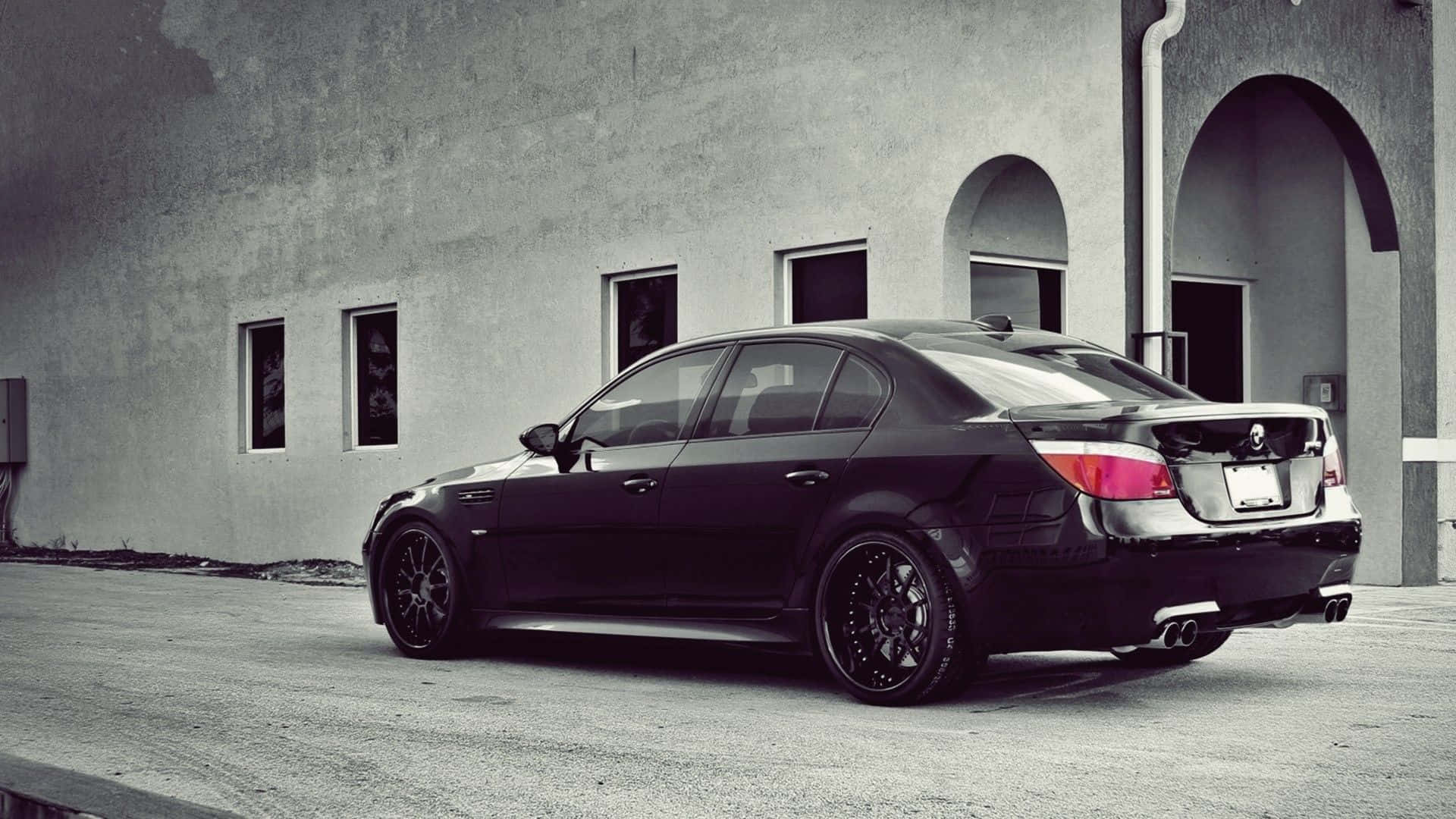 Bmw M5 桌布 壁紙 — 一輛時尚黑色BMW轎車配備訂製輪圈，停放在極簡混凝土建築前，建築帶有拱形窗戶。