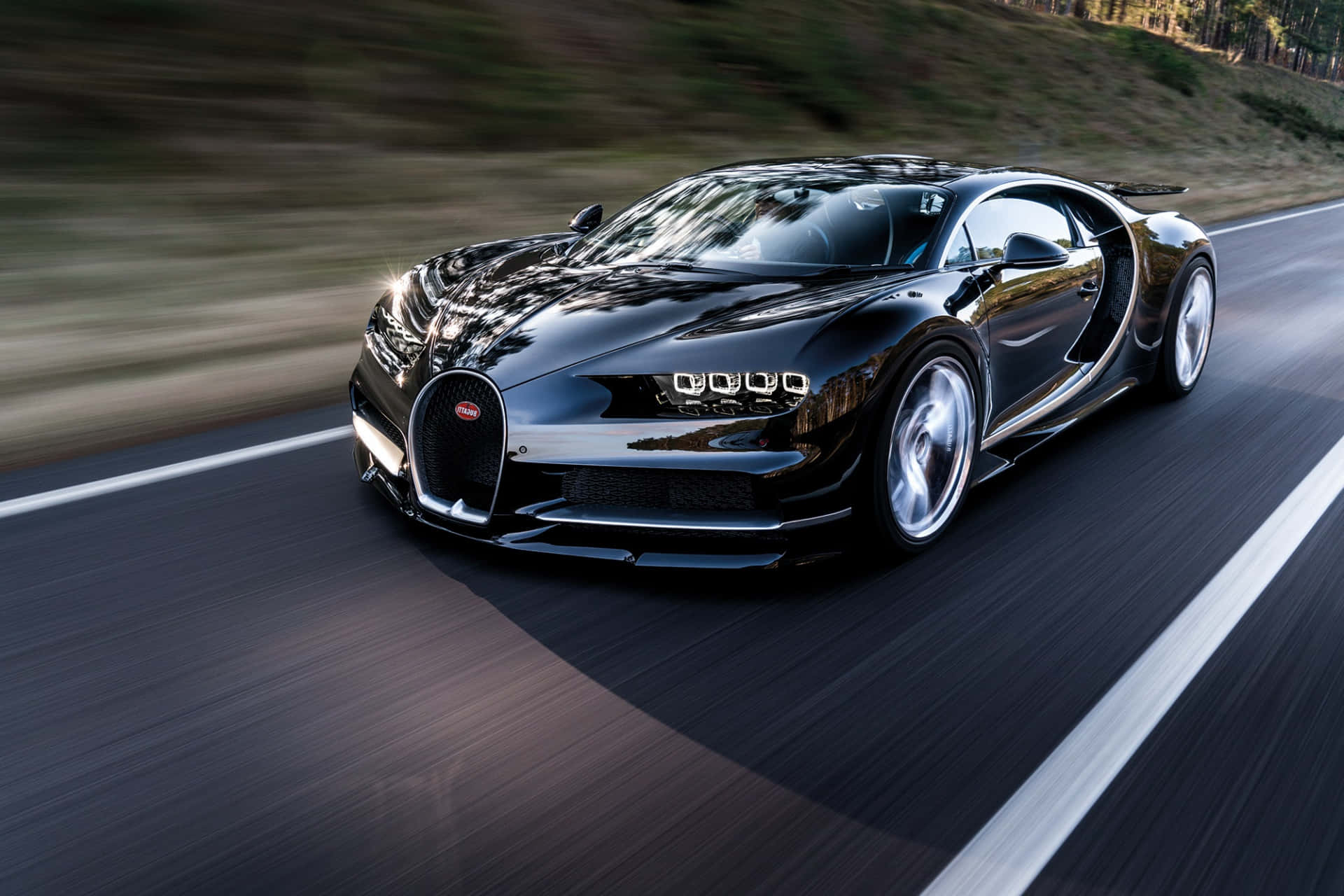 Bugatti Chiron 桌布 壁紙 — 一輛時尚的黑色Bugatti Chiron在蜿蜒的道路上疾馳，背景是模糊的森林景色。