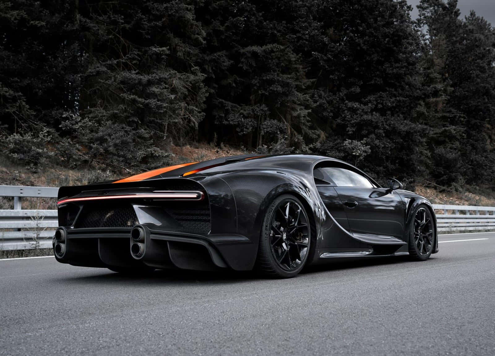 Bugatti Chiron 桌布 壁紙 — 一輛時尚的黑色Bugatti Chiron帶有橙色點綴，在陰天沿著森林道路飛馳。