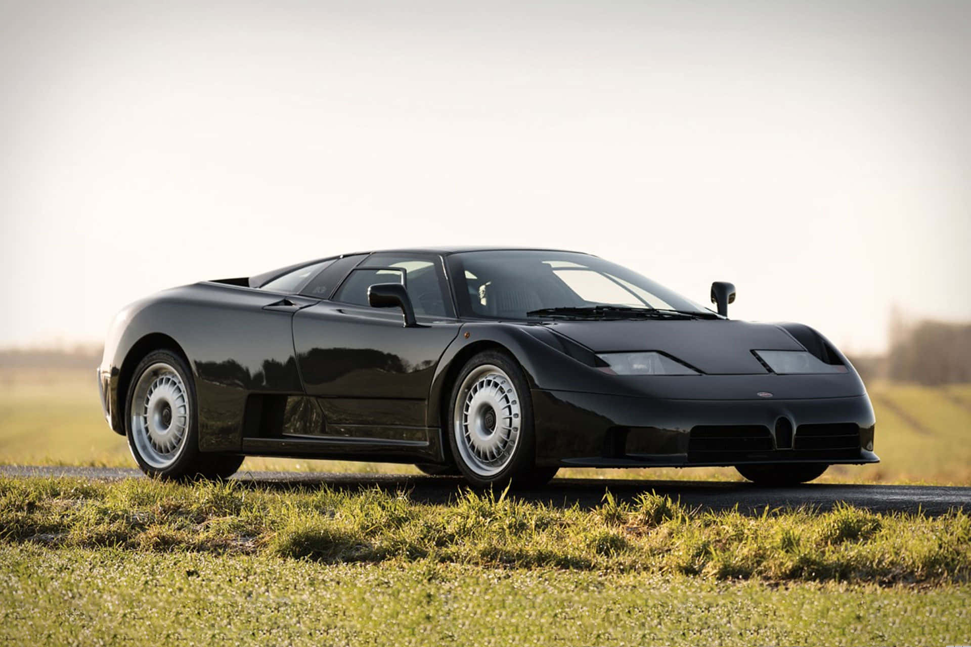 Bugatti Eb110 桌布 壁紙 — 一台流線型黑色Bugatti EB110超級跑車在柔和的金色時光下停泊在草地路邊。